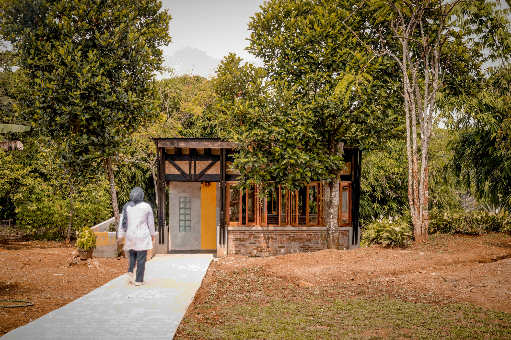 Visitor approaching the pavilion along the concrete walkway through the garden in afternoon light