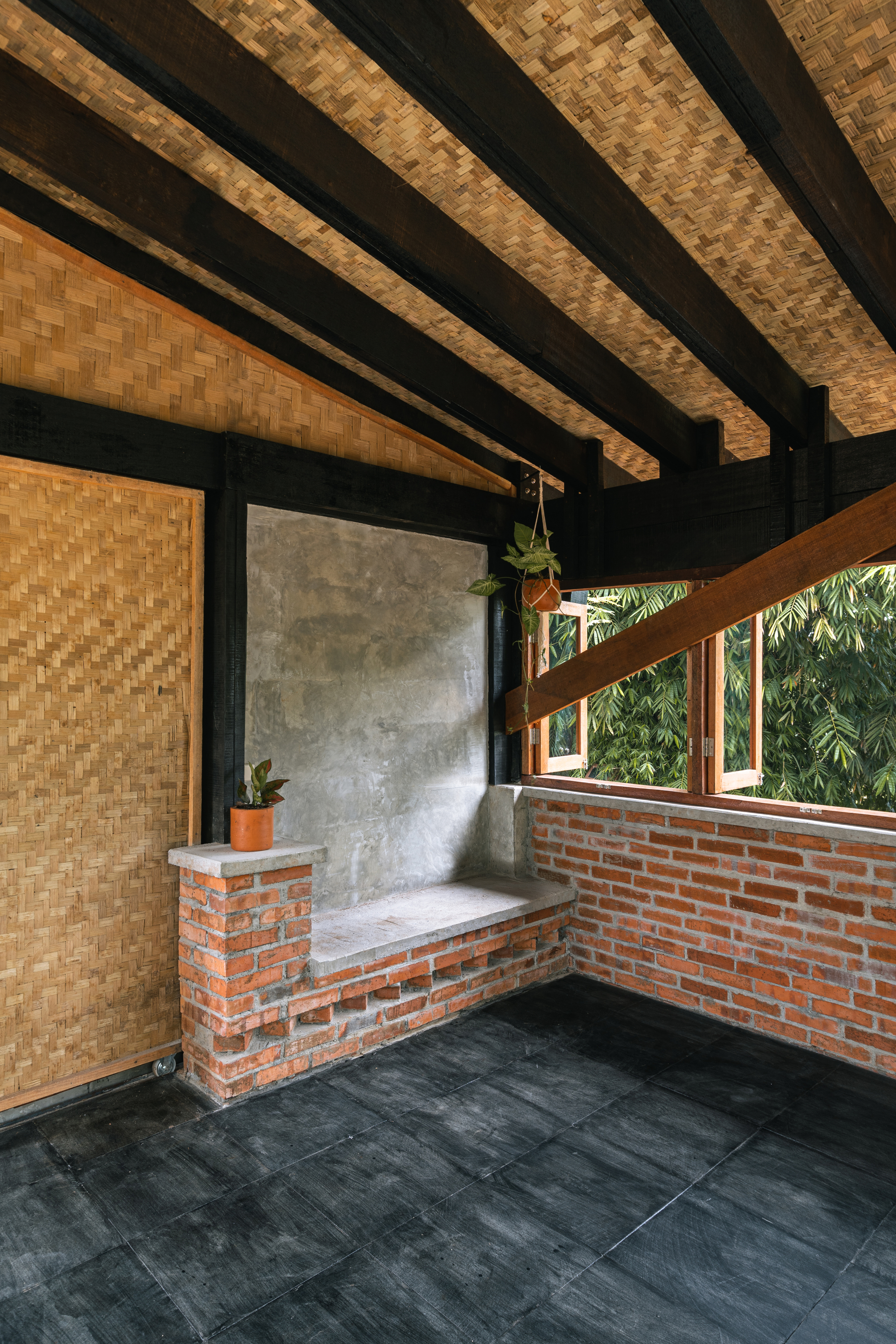 Corner seating nook with concrete-rendered wall and brick base under bamboo ceiling