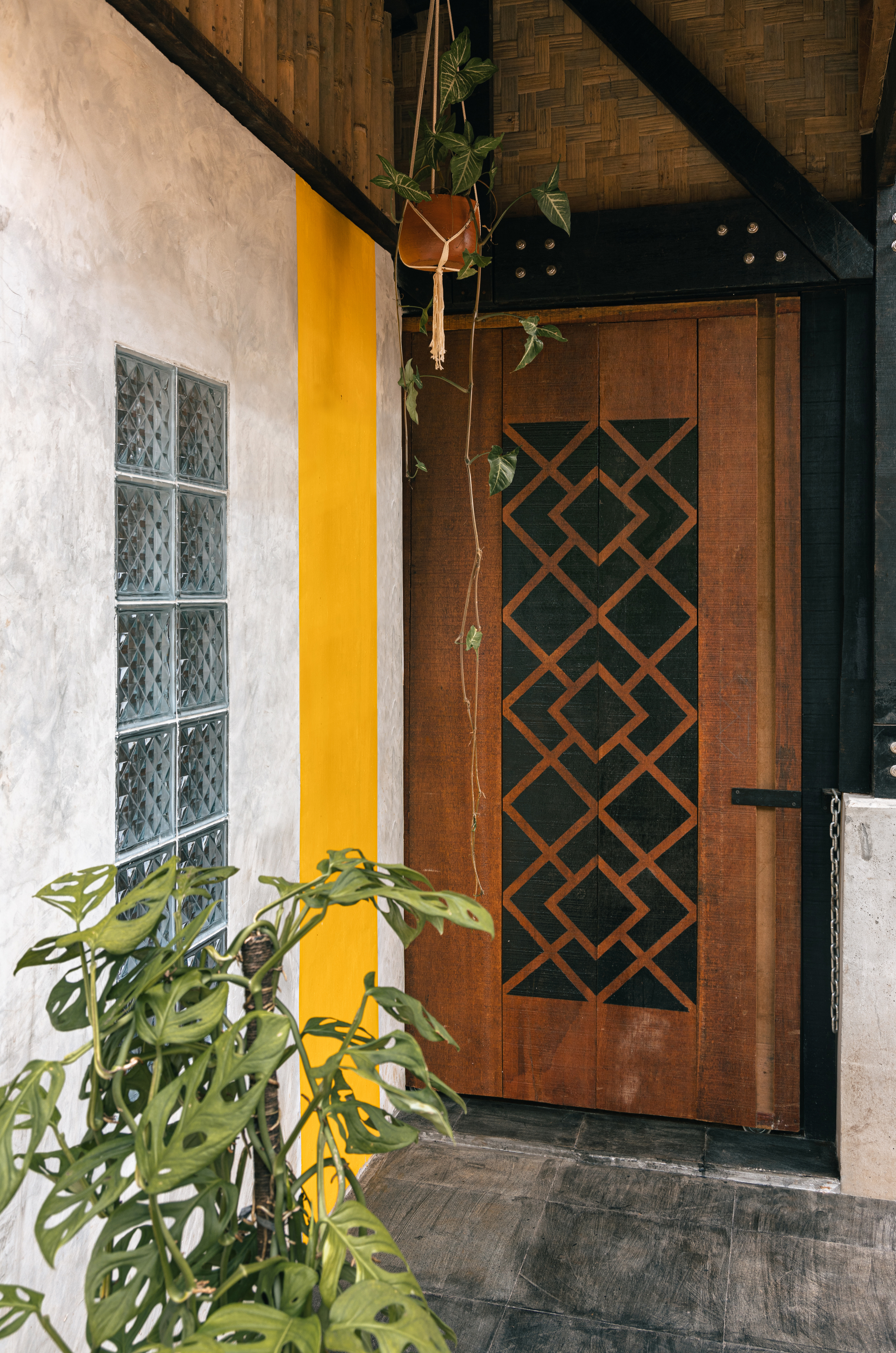 Entrance with geometric lattice timber door beneath a woven bamboo ceiling and hanging potted plants