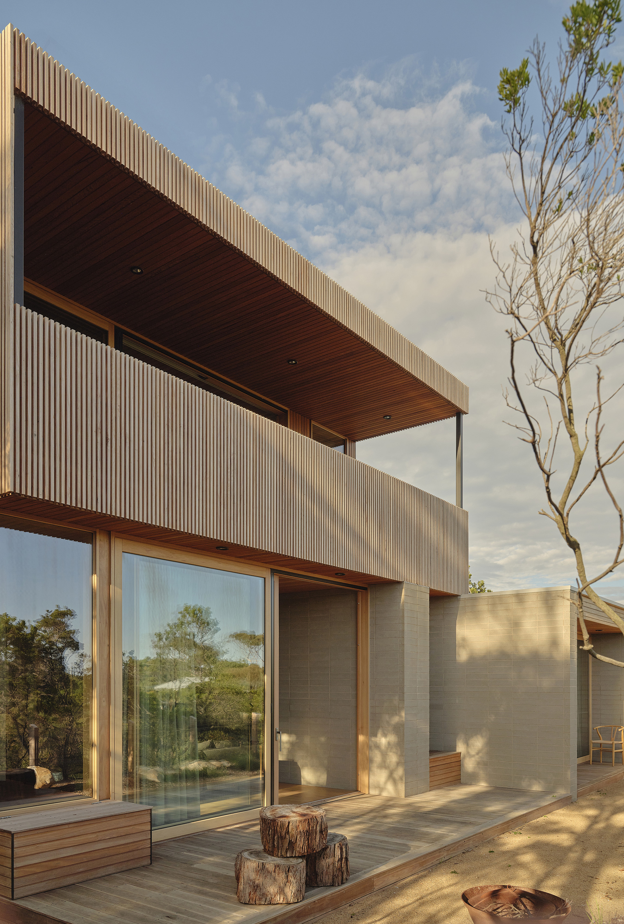 Corner terrace with cantilevered timber soffit and glass sliding doors framed by tree stumps