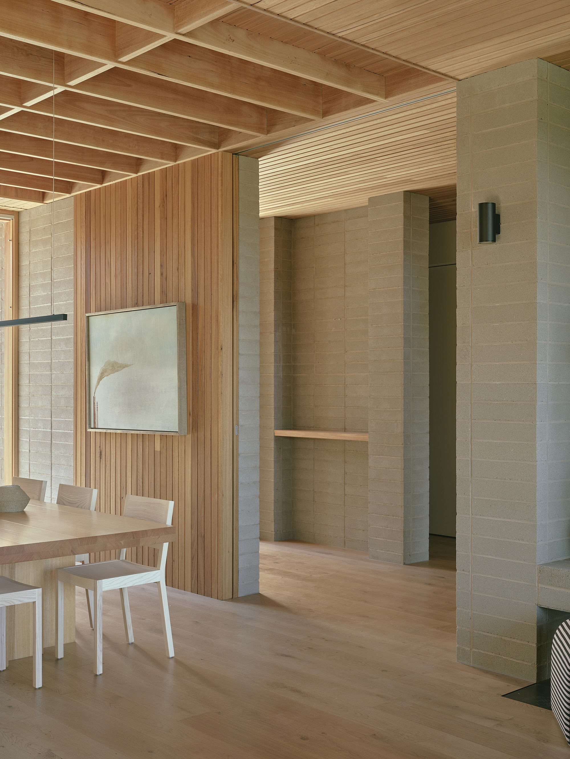 Interior with exposed timber ceiling joists and rammed earth walls flanking a passage to dining area