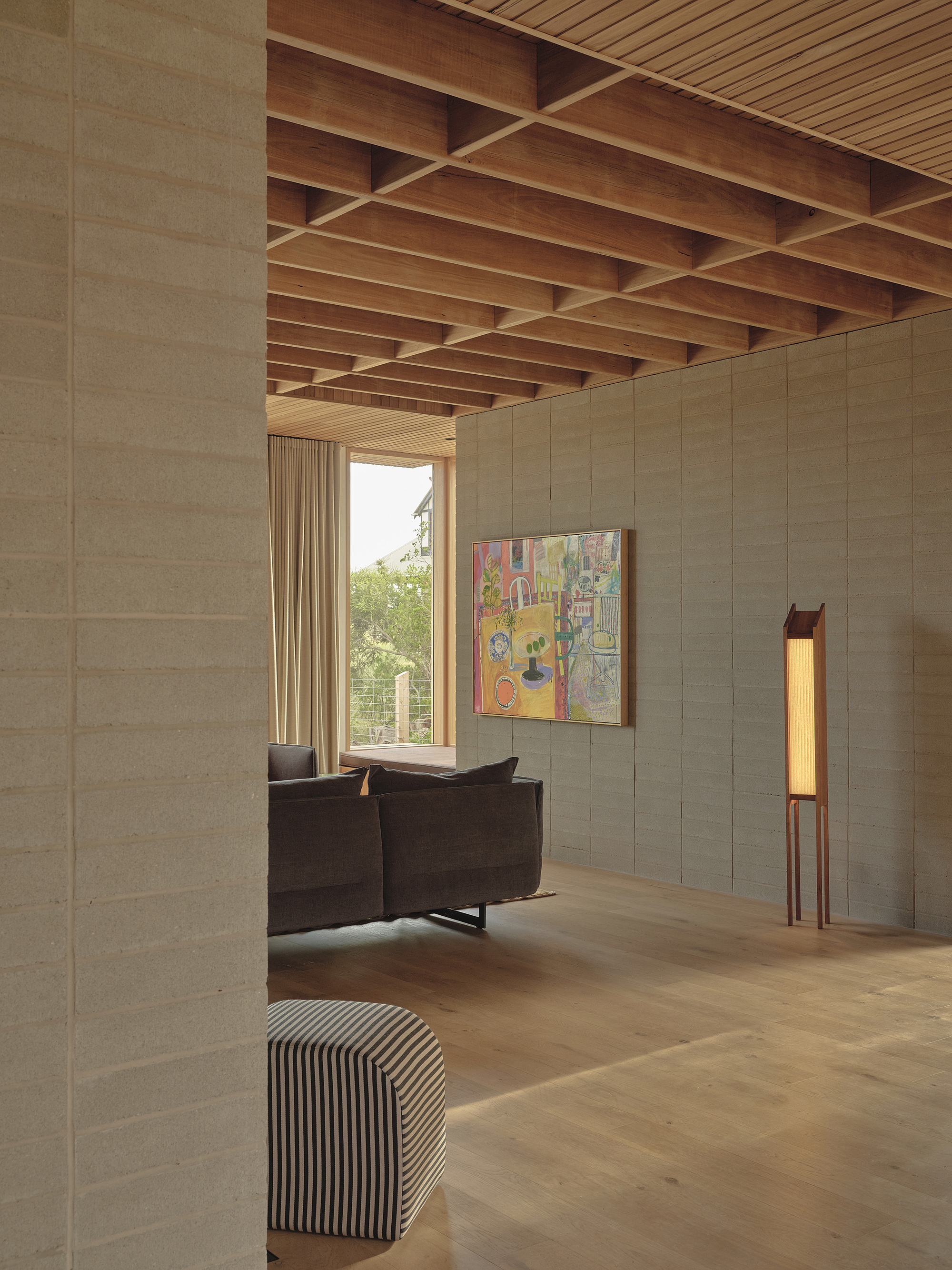 Interior living space with exposed timber beam ceiling and textured block wall opening to trees
