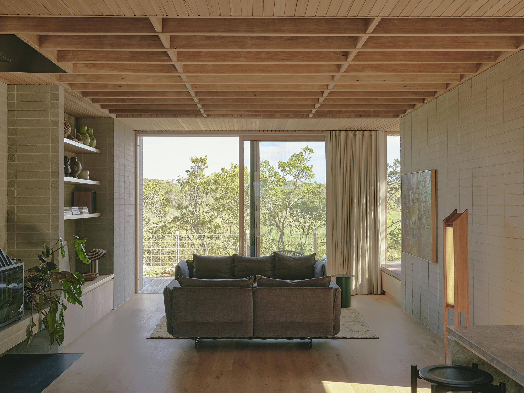 Living room framing floor-to-ceiling glazing that looks onto woodland with exposed timber joists above