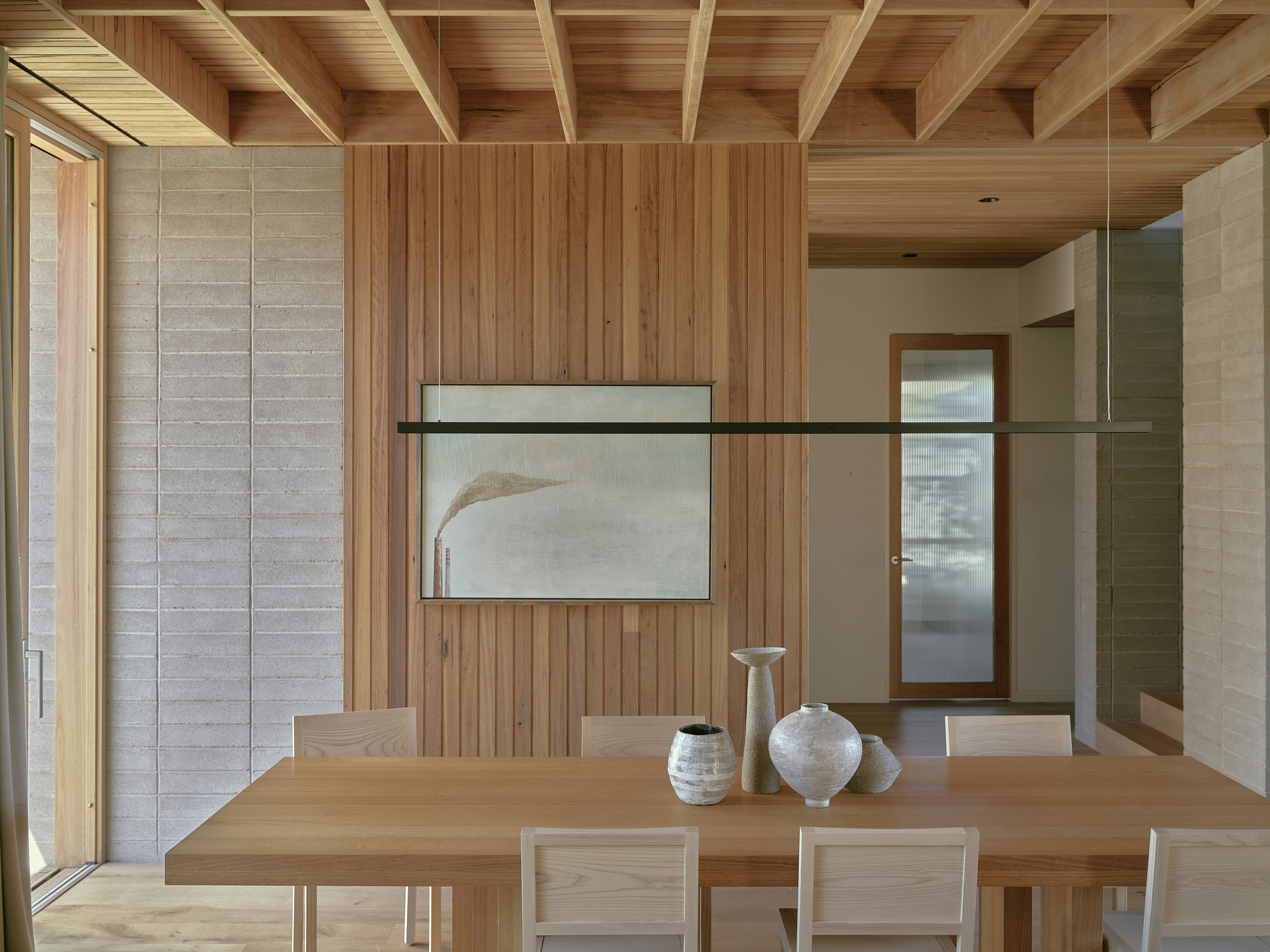 Dining area with timber-clad walls and exposed beam ceiling beneath a suspended linear light fixture
