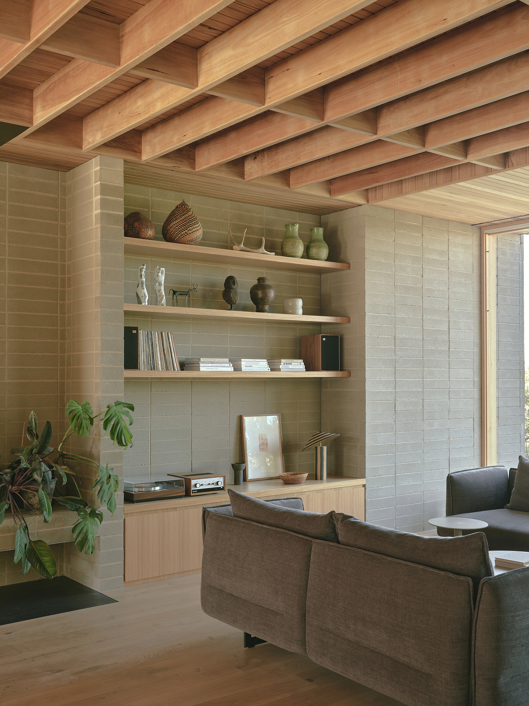 Built-in timber shelving with exposed beam ceiling and textured masonry wall beside a potted plant