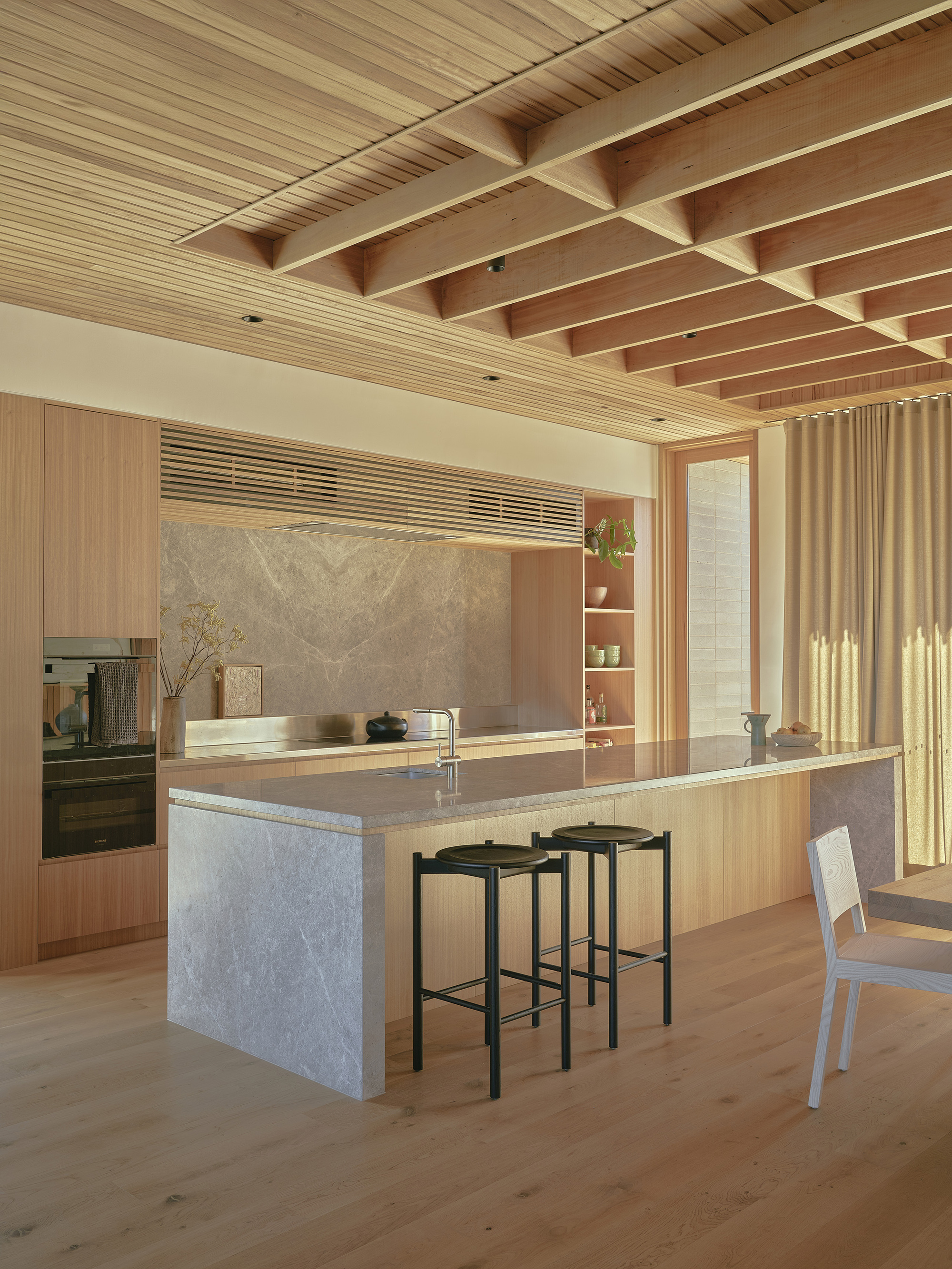 Kitchen island with stone base and timber joinery beneath exposed timber beams and slatted ceiling
