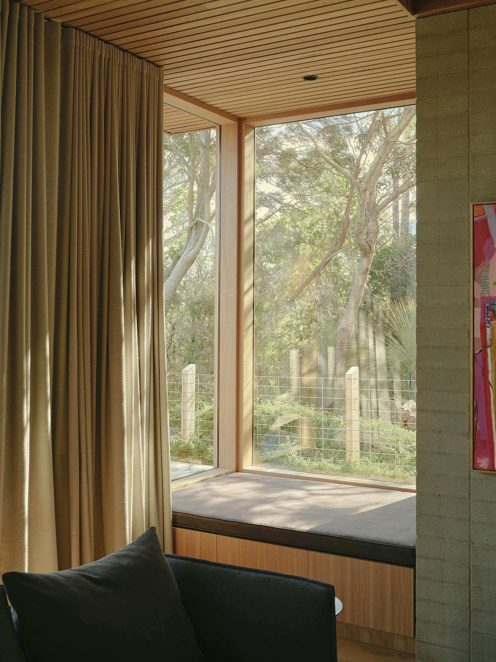 Window seat with timber frame and glazing overlooking garden trees in afternoon light