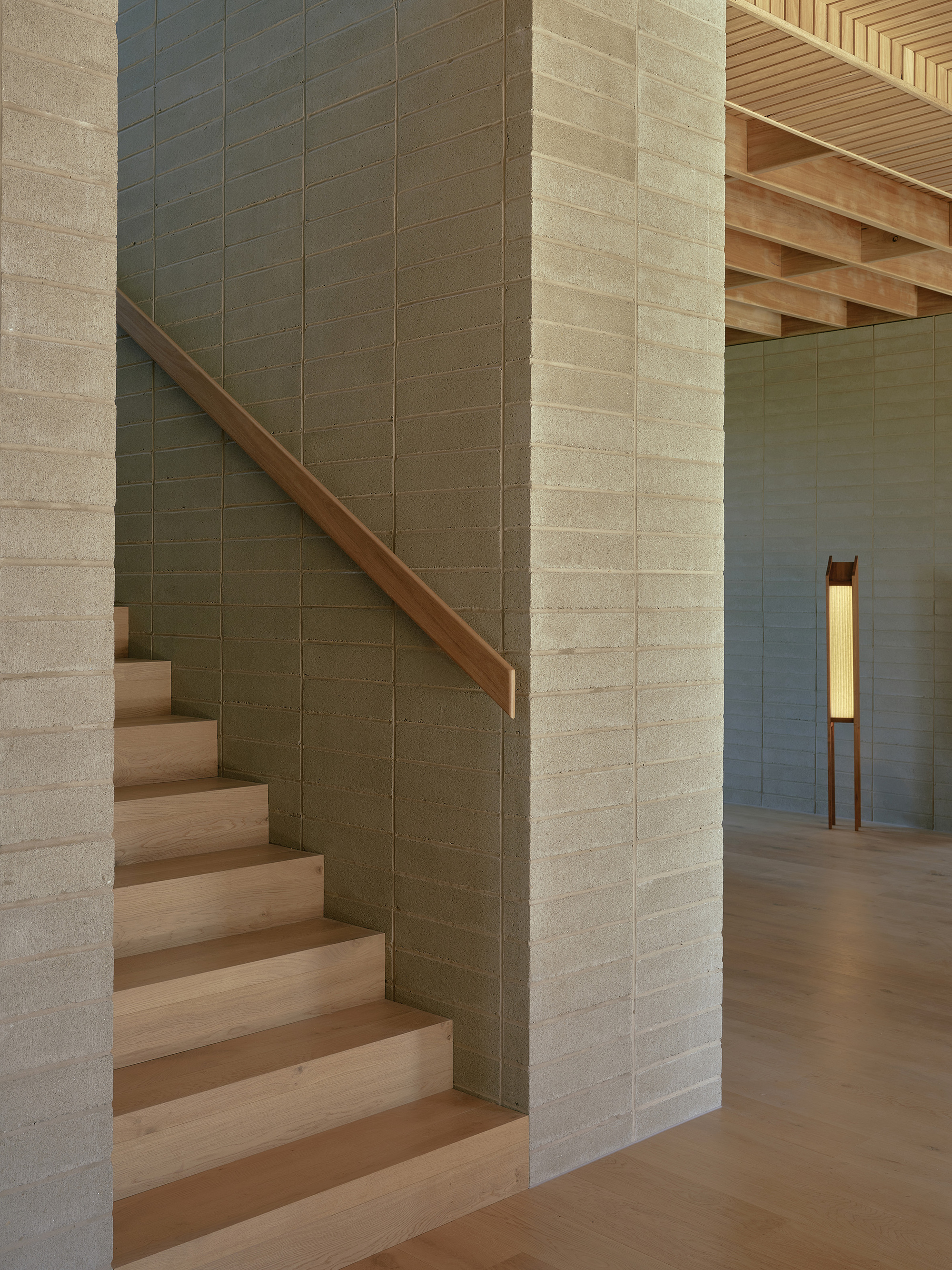 Timber stair with stone tile wall rising past exposed ceiling joists and floor lamp