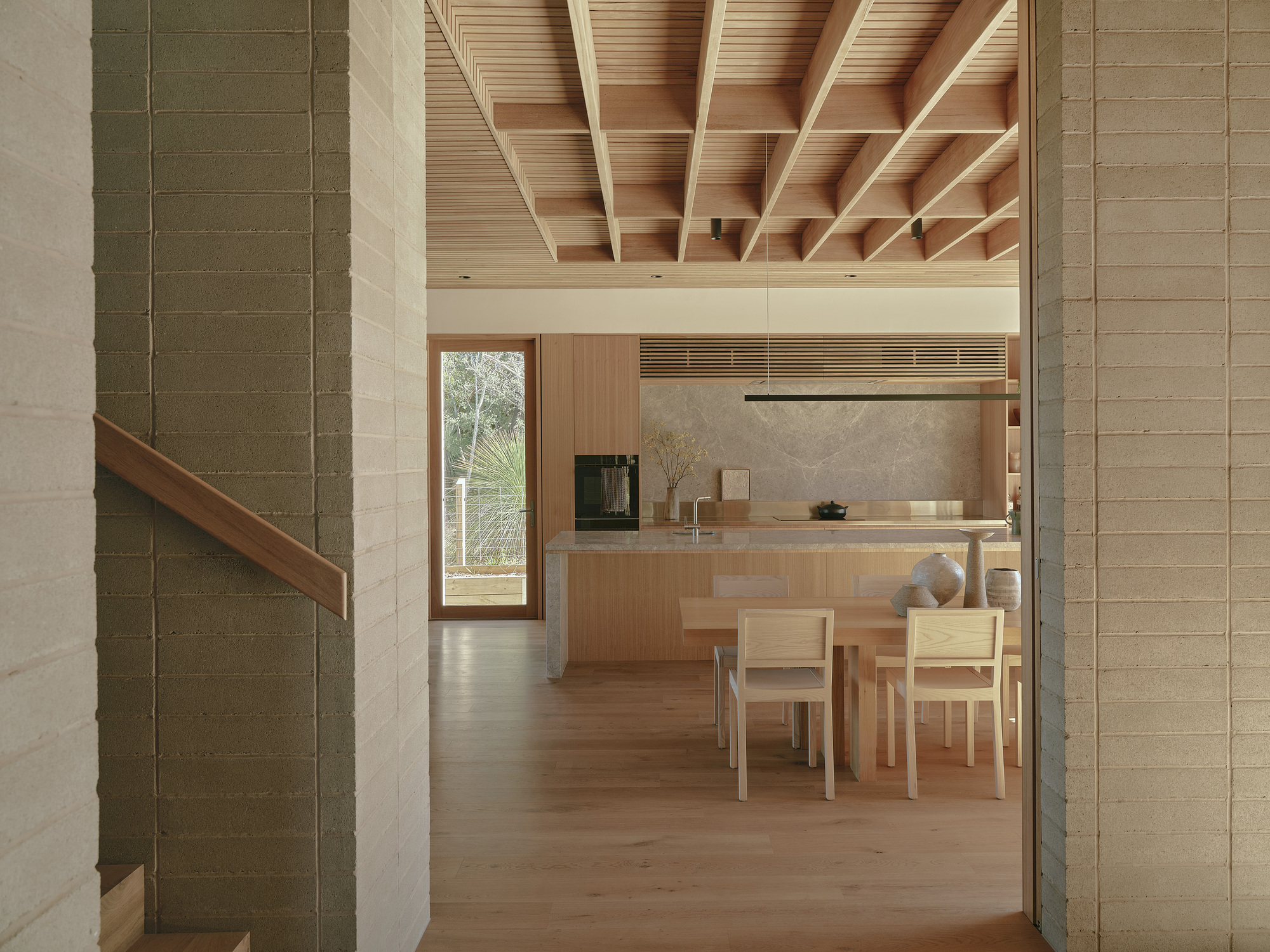View through stone tile columns into kitchen and dining area with exposed timber ceiling structure