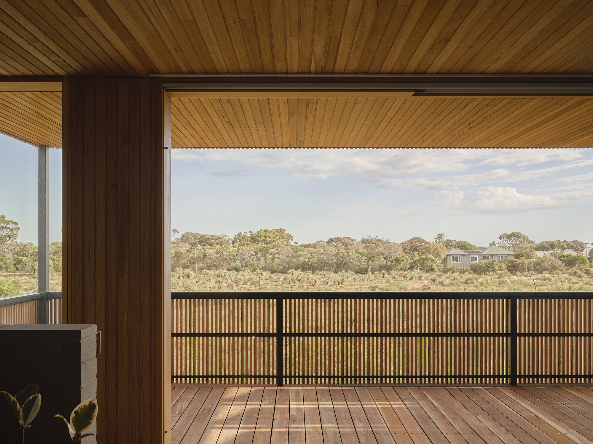 Timber deck with slatted balustrade overlooking native bushland under partly cloudy sky