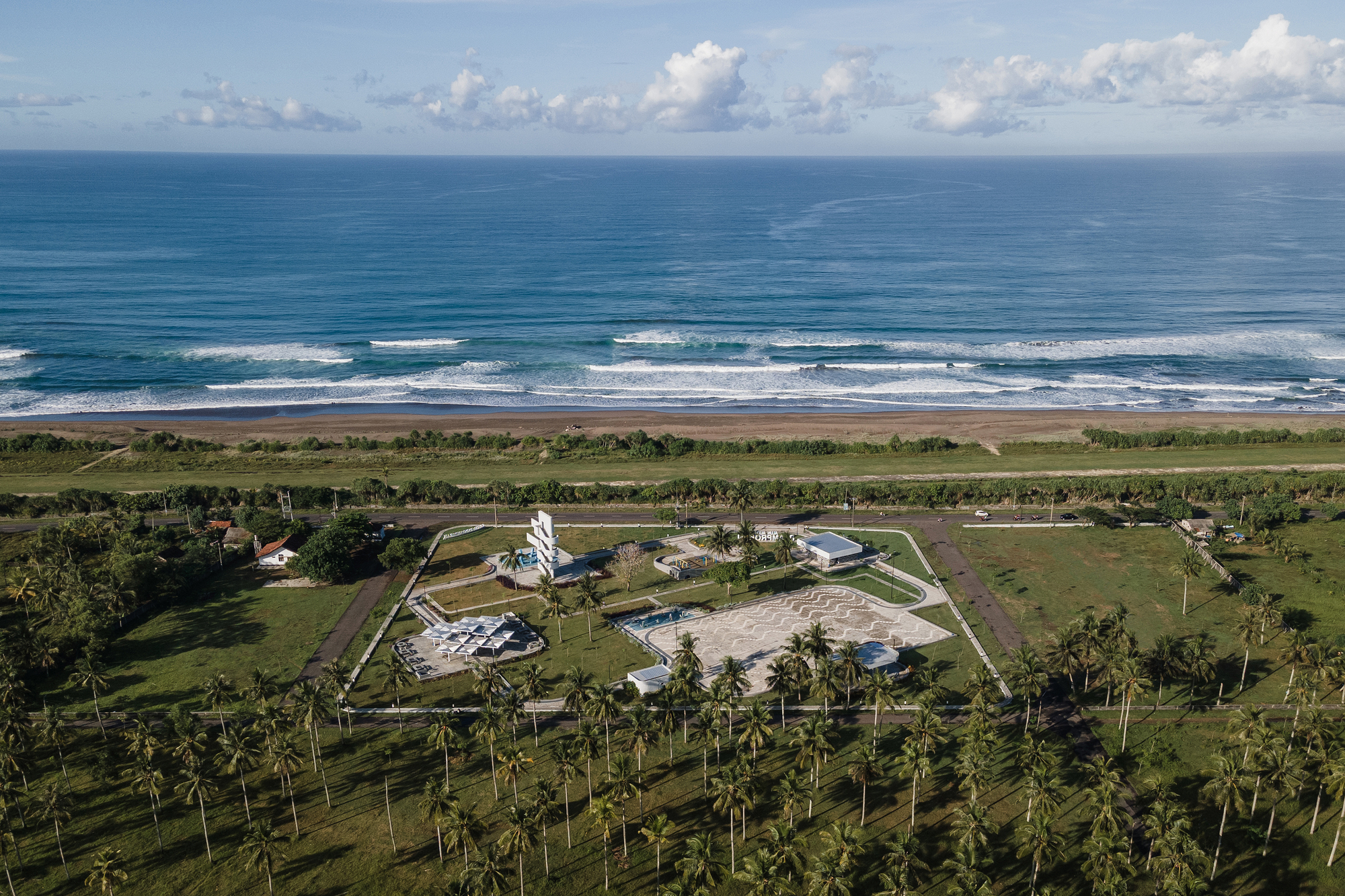 Aerial view of the coastal compound with palm groves and ocean surf beyond green fields