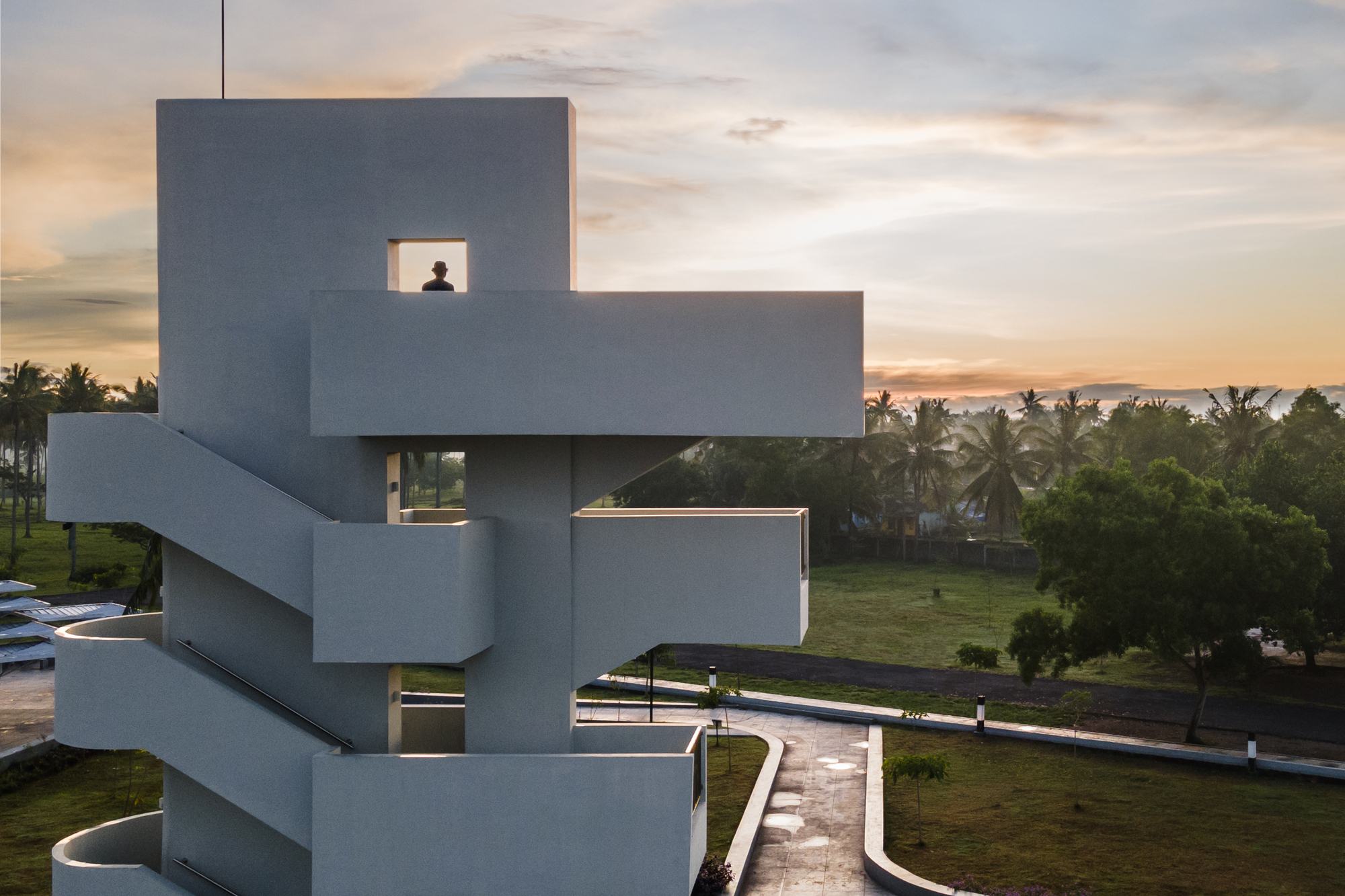 Stacked concrete viewing tower with cutout windows and exterior staircase at dusk