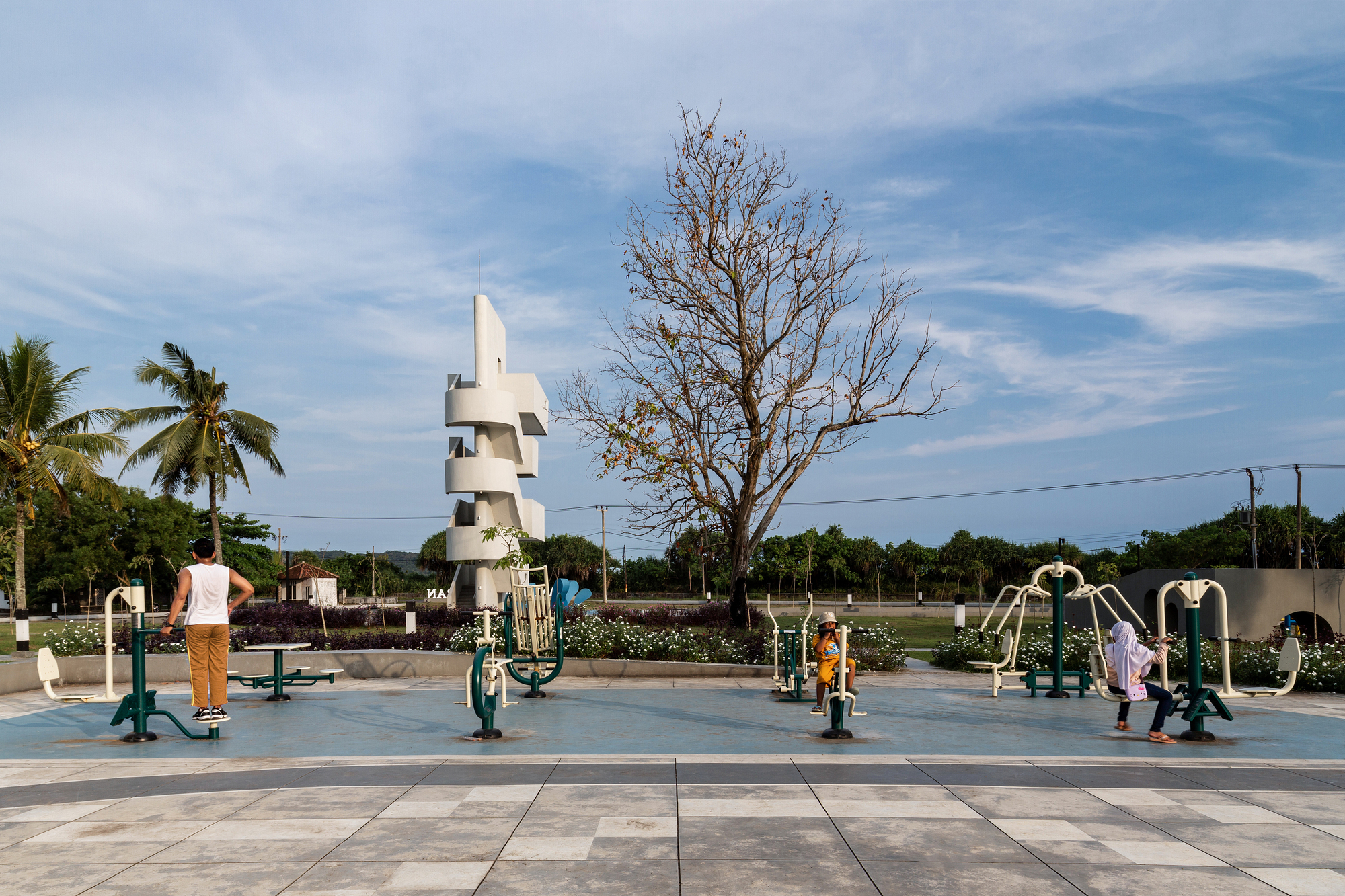 Outdoor exercise equipment area with spiraling white tower and visitors beneath a bare tree