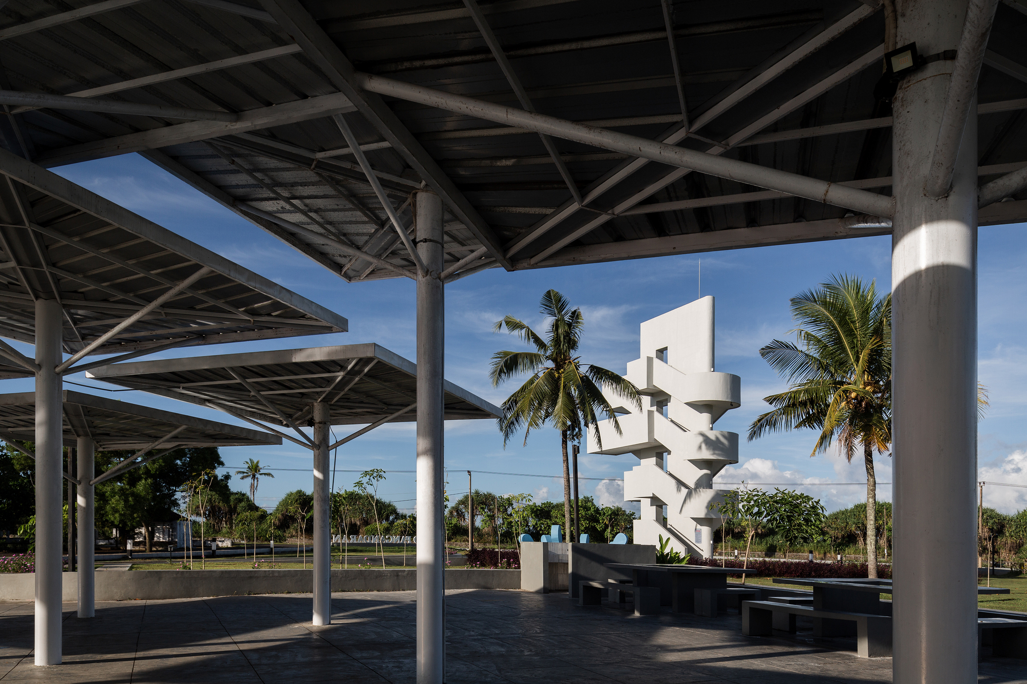 View from beneath the gridded steel canopy toward the white spiraling tower and palm trees