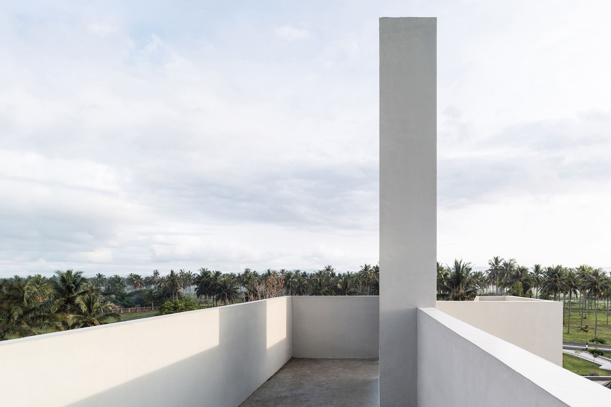 Rooftop terrace with tall square chimney rising above parapets and palm grove below