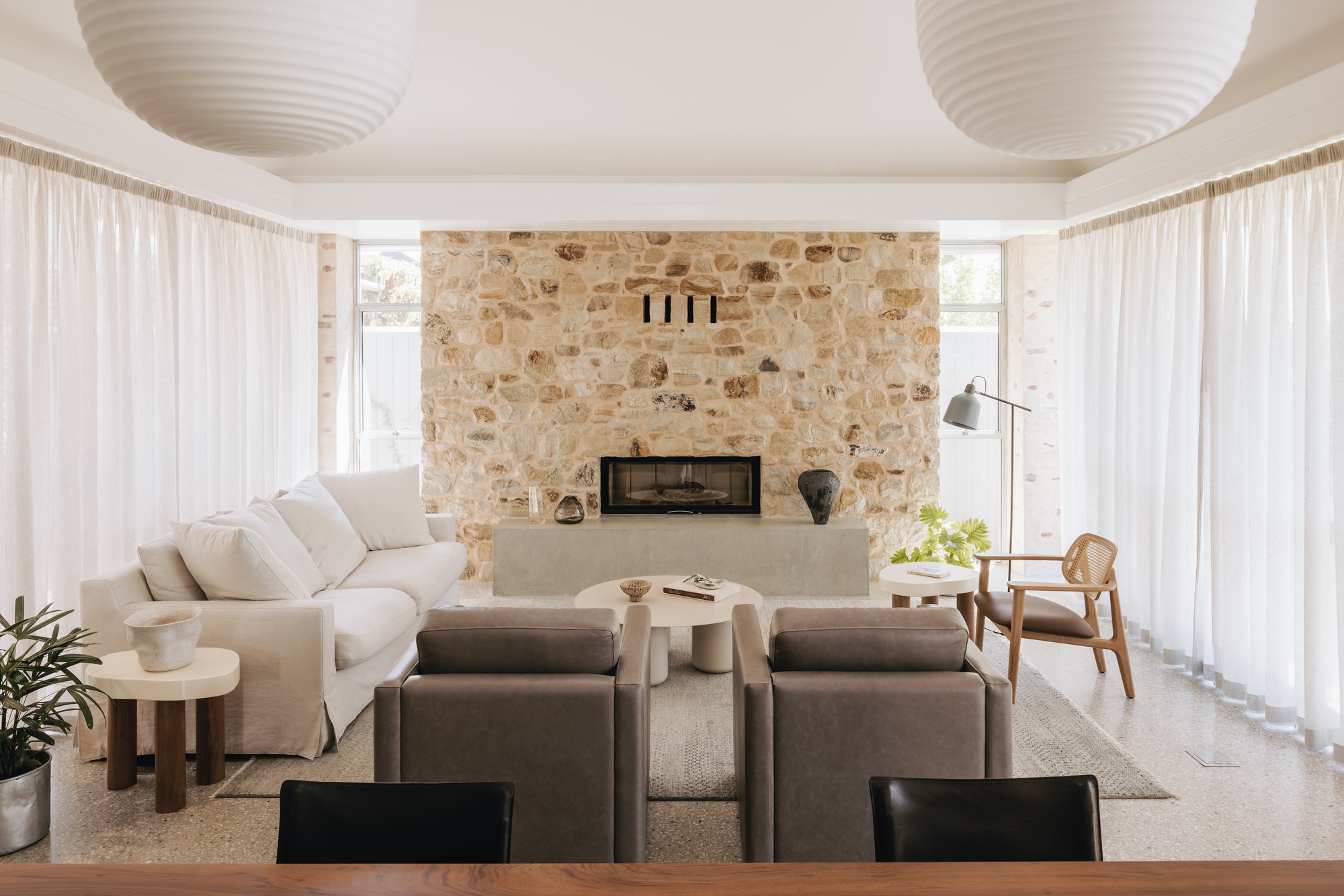 Living room with sandstone fireplace wall flanked by sheer curtains and two paper lanterns overhead