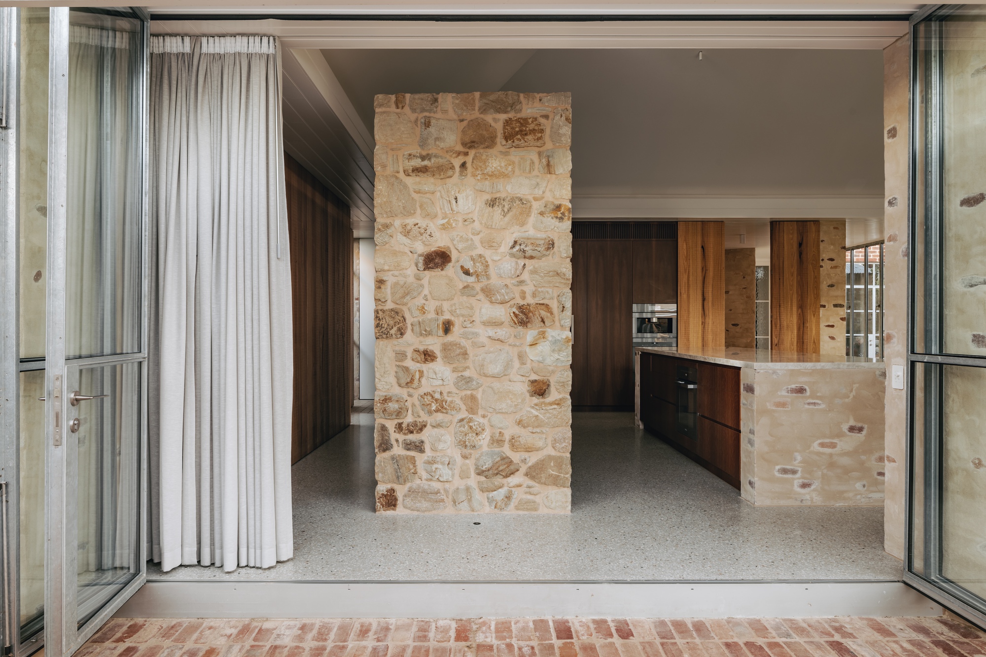 View through open glass doors to kitchen with freestanding sandstone wall and terrazzo flooring