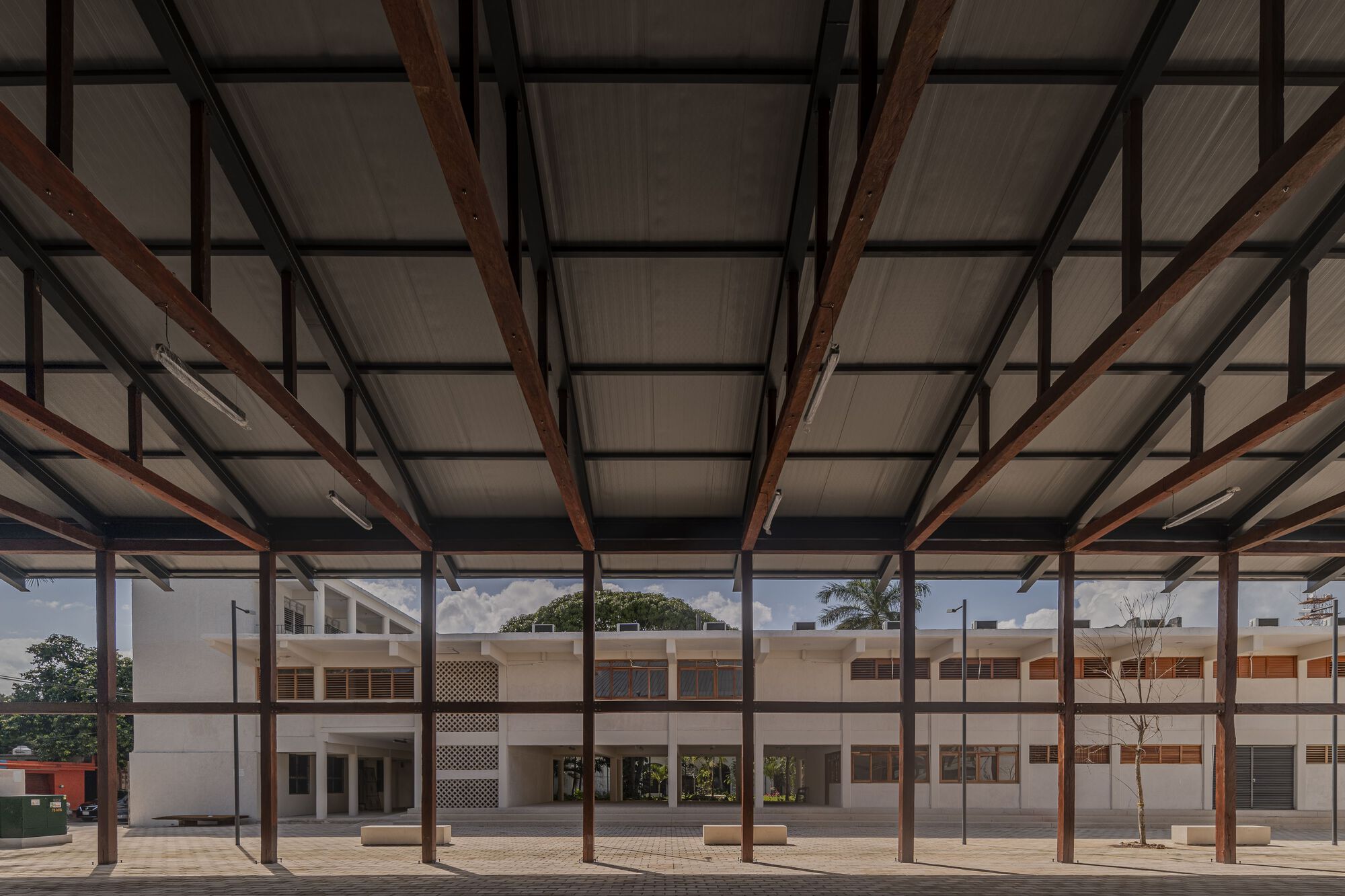 Covered open-air hall with exposed timber beams and steel columns framing the courtyard beyond