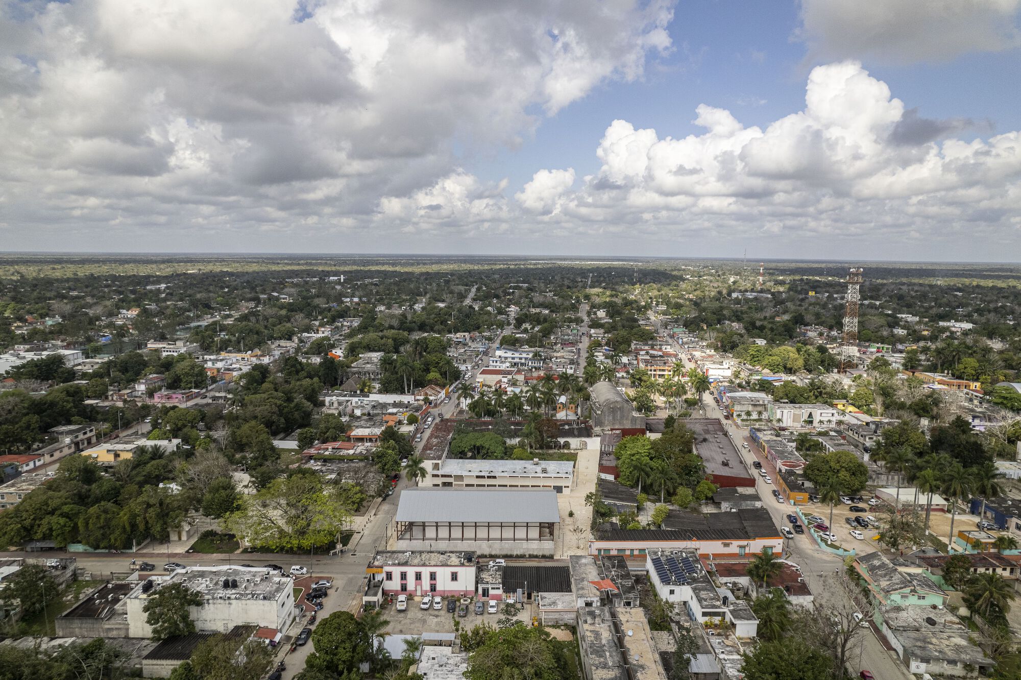 Drone view of the warehouse-style building with expansive glazed facade rising above surrounding neighborhood rooftops under cloudy skies