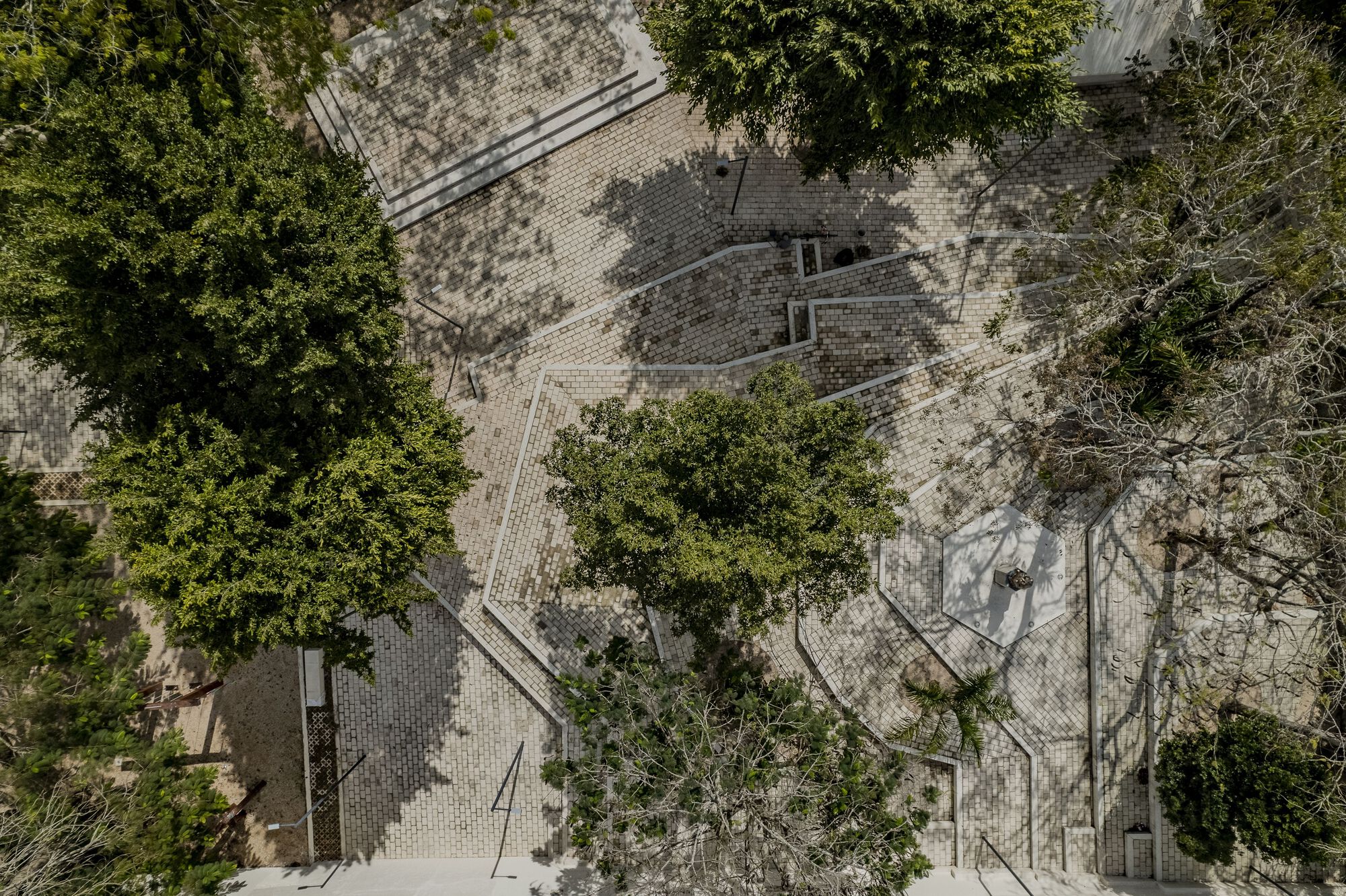 Overhead view of paved plaza with stone pavers, curved pathways, and trees casting dappled shadows