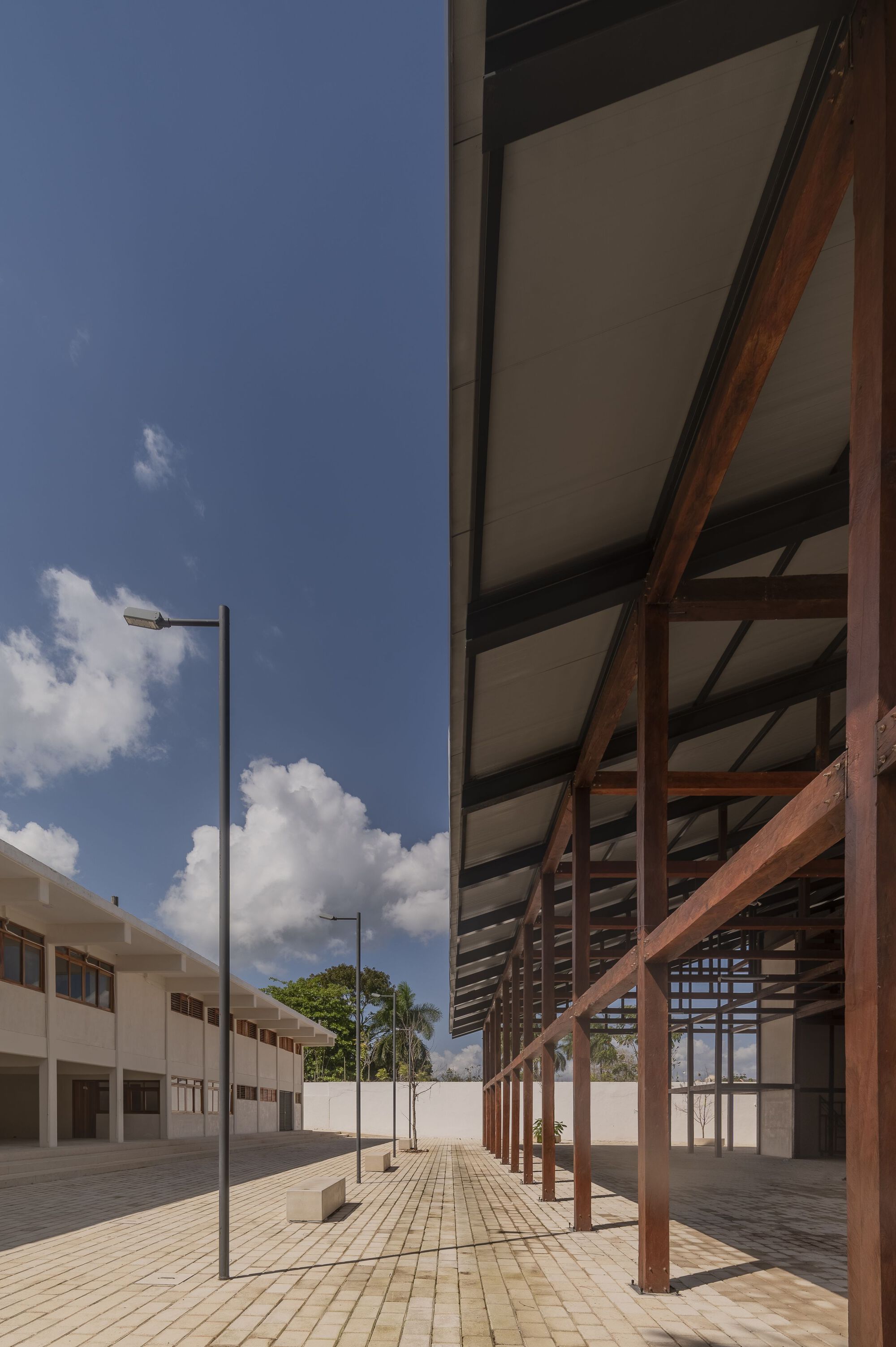 Timber colonnade with diagonal bracing and pale ceiling panels adjacent to a tiled courtyard