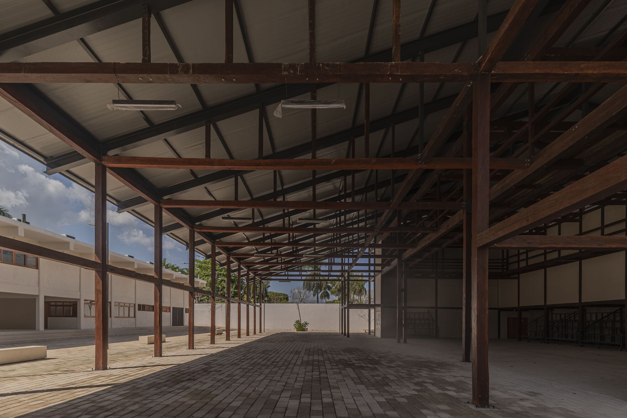Covered corridor with timber post-and-beam structure framing views to a planted courtyard beyond