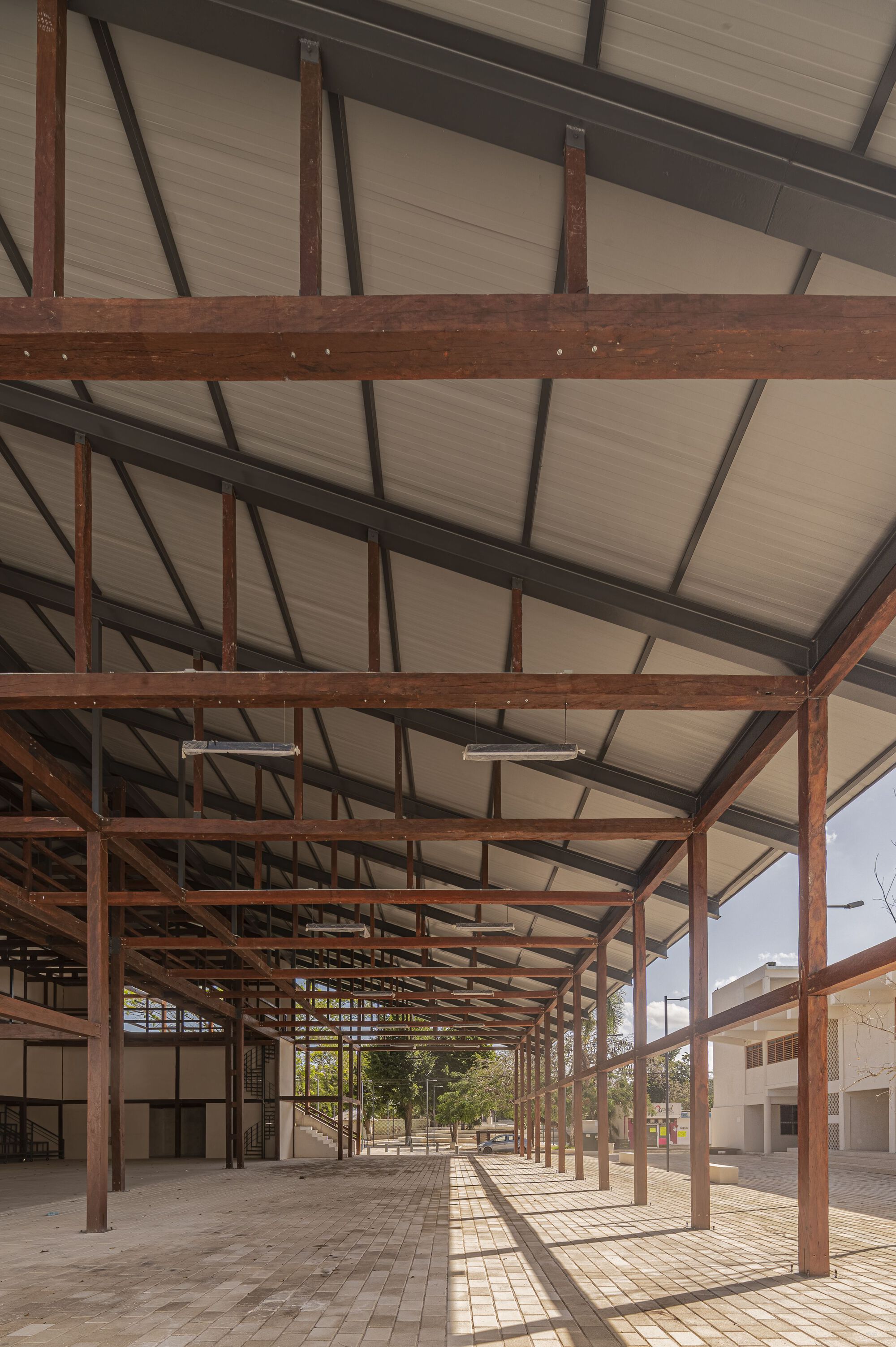 Long perspective through the open-sided covered walkway with brick paving and dappled afternoon shadows
