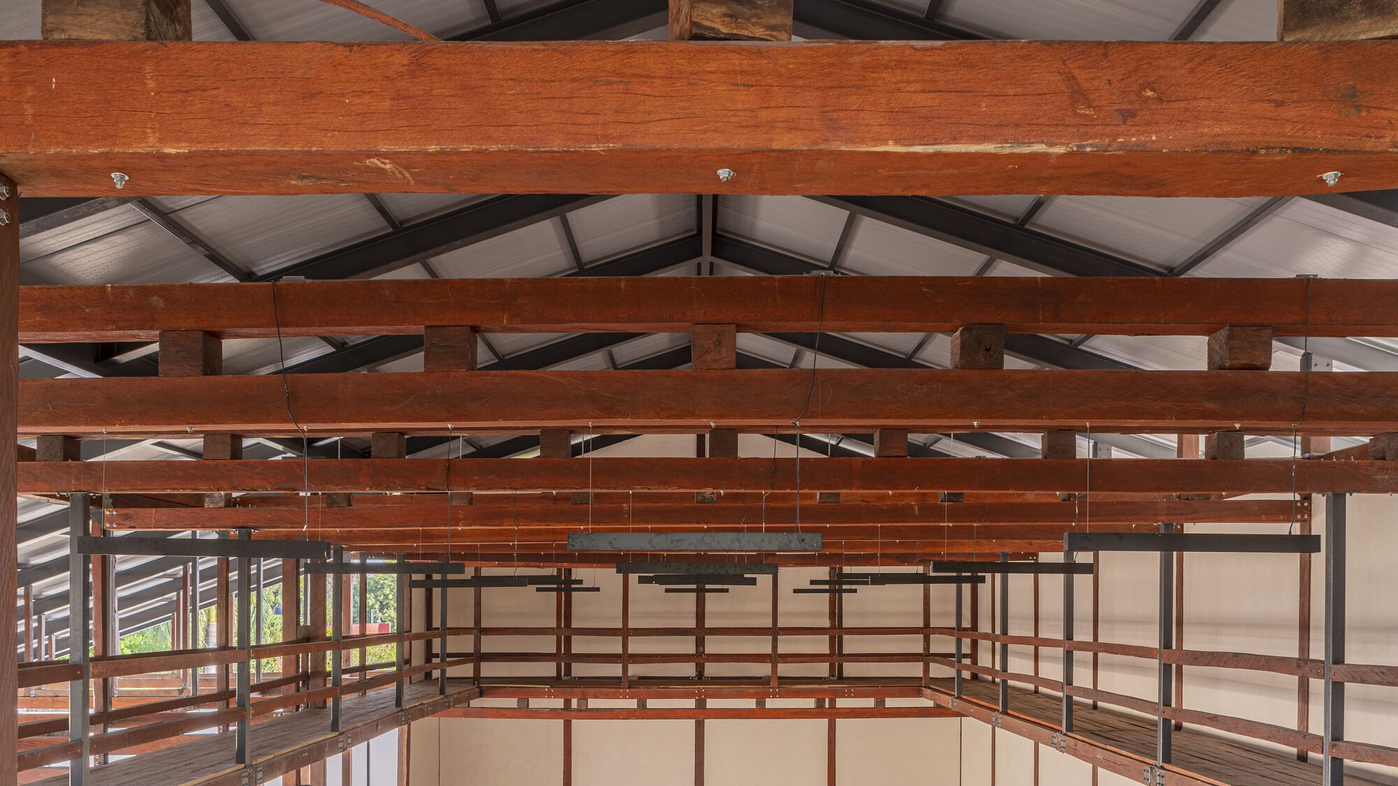 Interior view of layered timber beams and metal railing system beneath a translucent panel ceiling