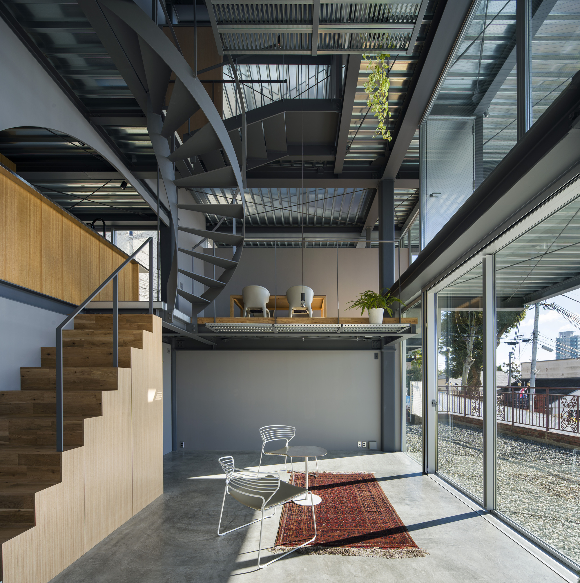 Triple-height interior with spiral staircase and stacked mezzanine platforms beneath a slatted ceiling open to sky