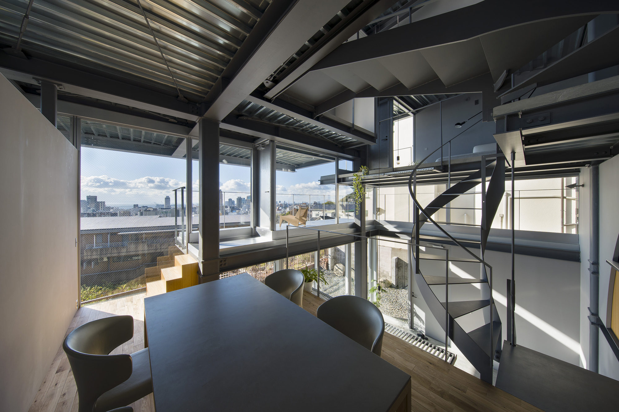 Open-plan dining area with exposed steel structure and spiral staircase overlooking the rooftop terrace