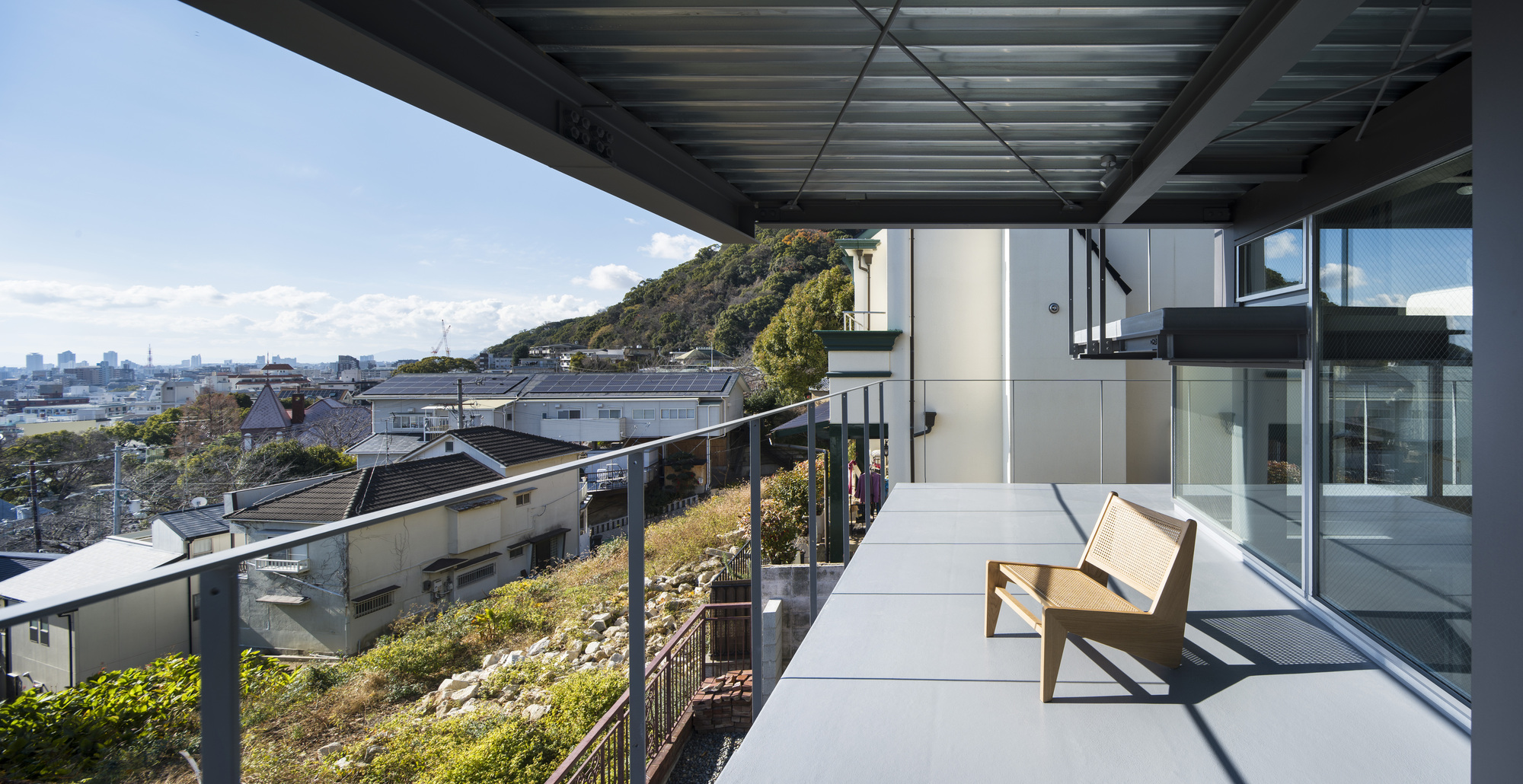 Rooftop terrace with steel canopy, timber bench, and planted green roof overlooking the hillside neighborhood