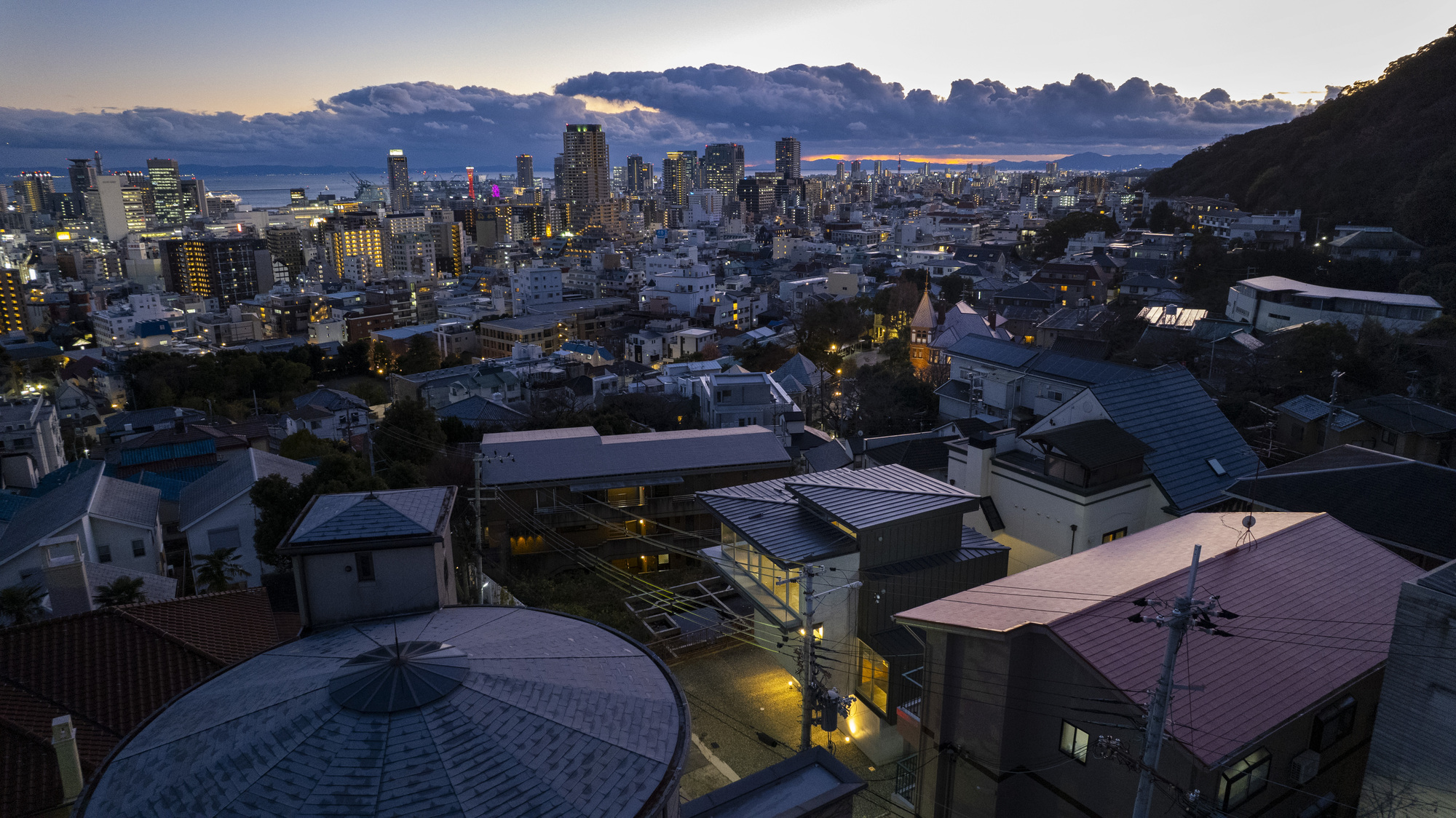 Aerial view of residential volumes with varied metal roofs nestled in a hillside neighborhood at dusk