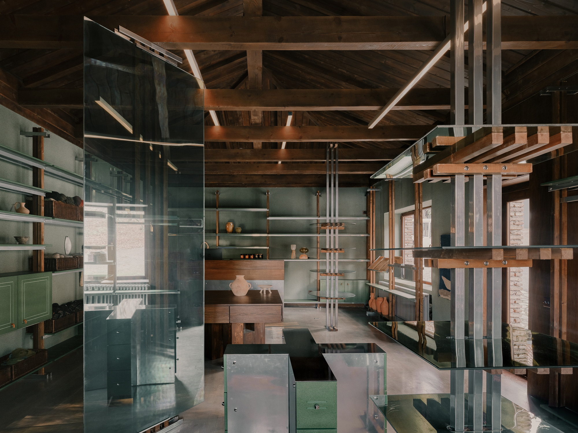 Interior with exposed timber roof beams, glass partitions, and timber and metal shelving systems under soft daylight