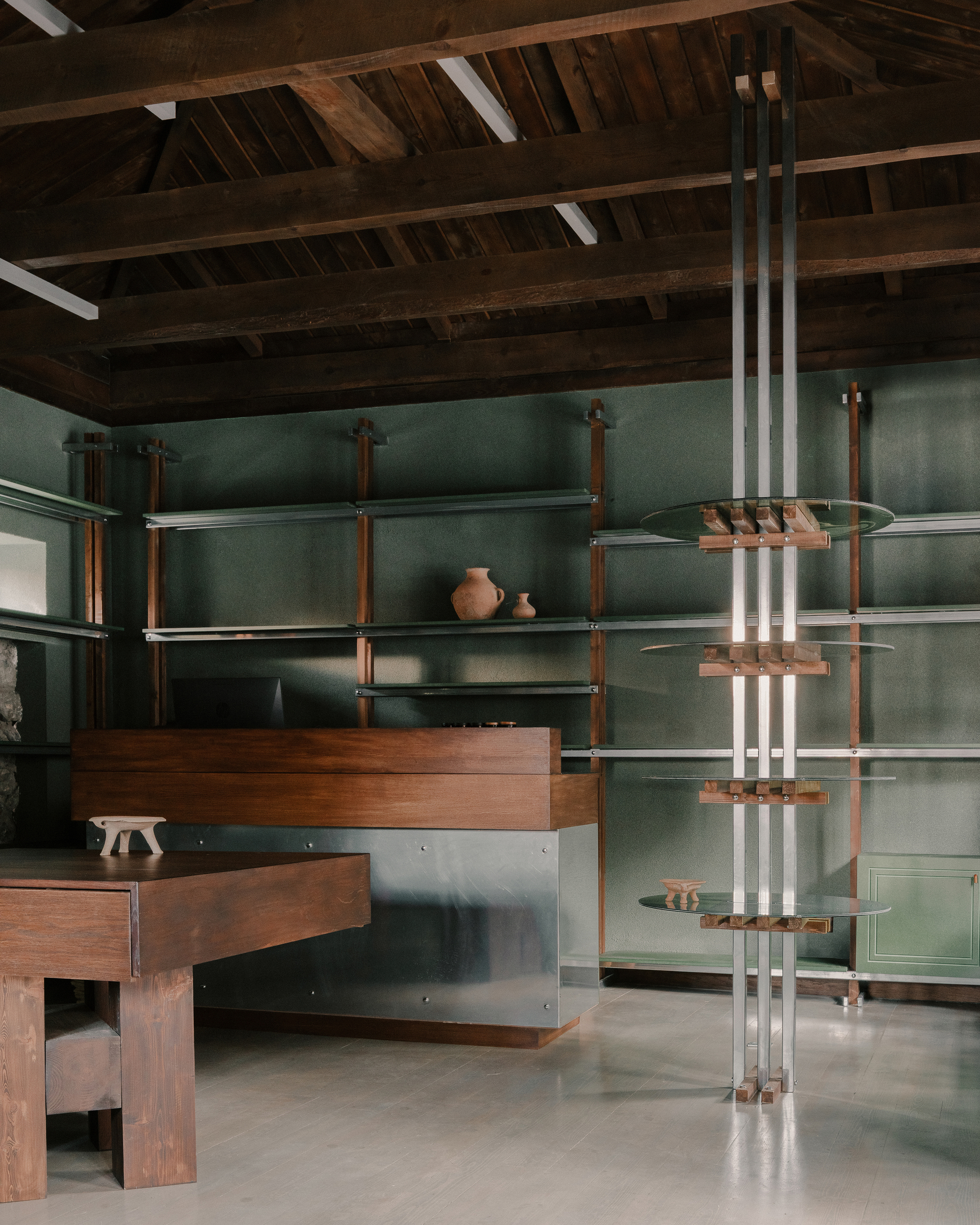 Interior retail space with exposed timber beams, green panels, timber and stainless steel shelving units, and ceramic pottery