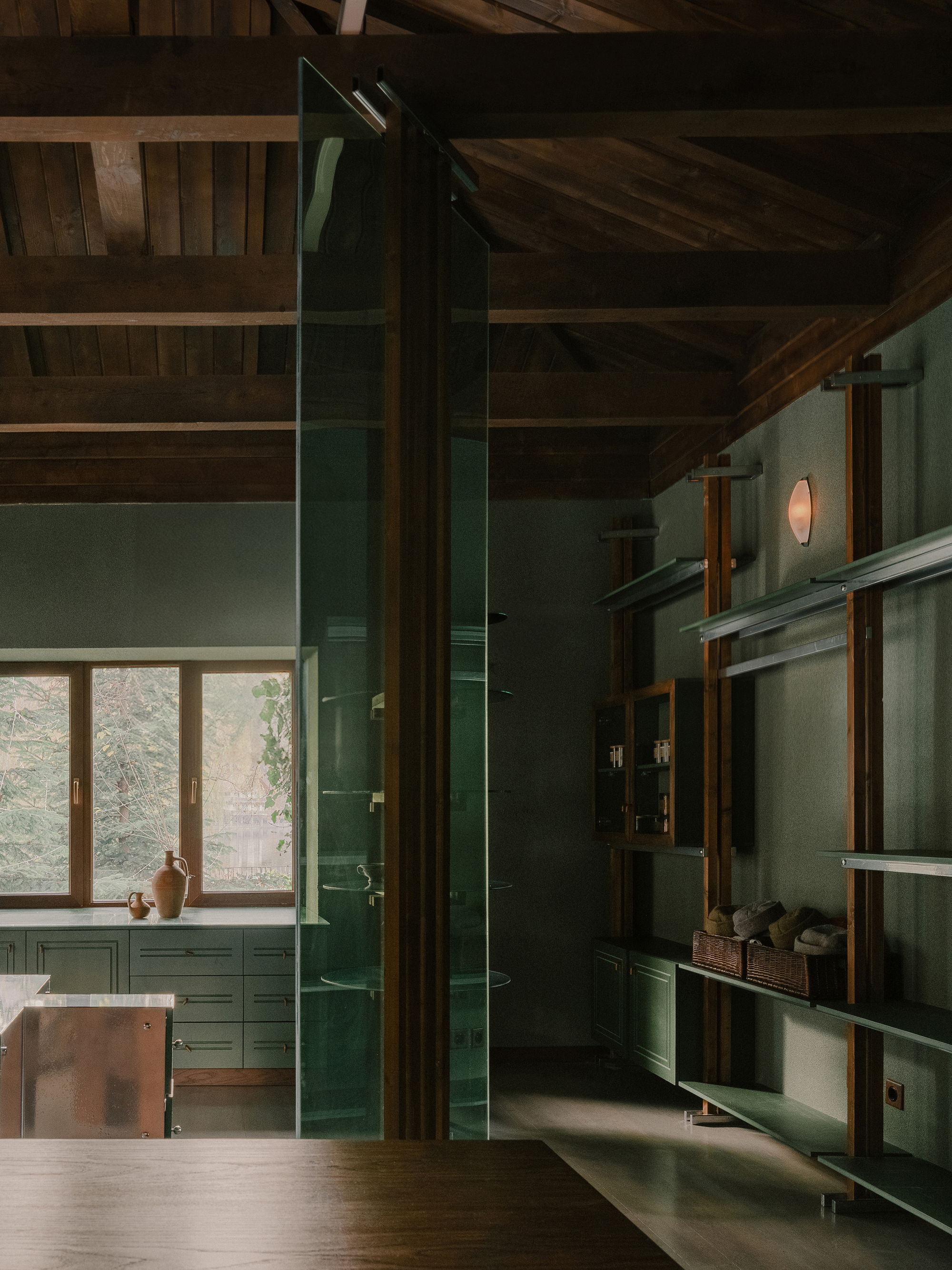 Tall green glazed partition wall beneath exposed timber rafters with natural light filtering through windows