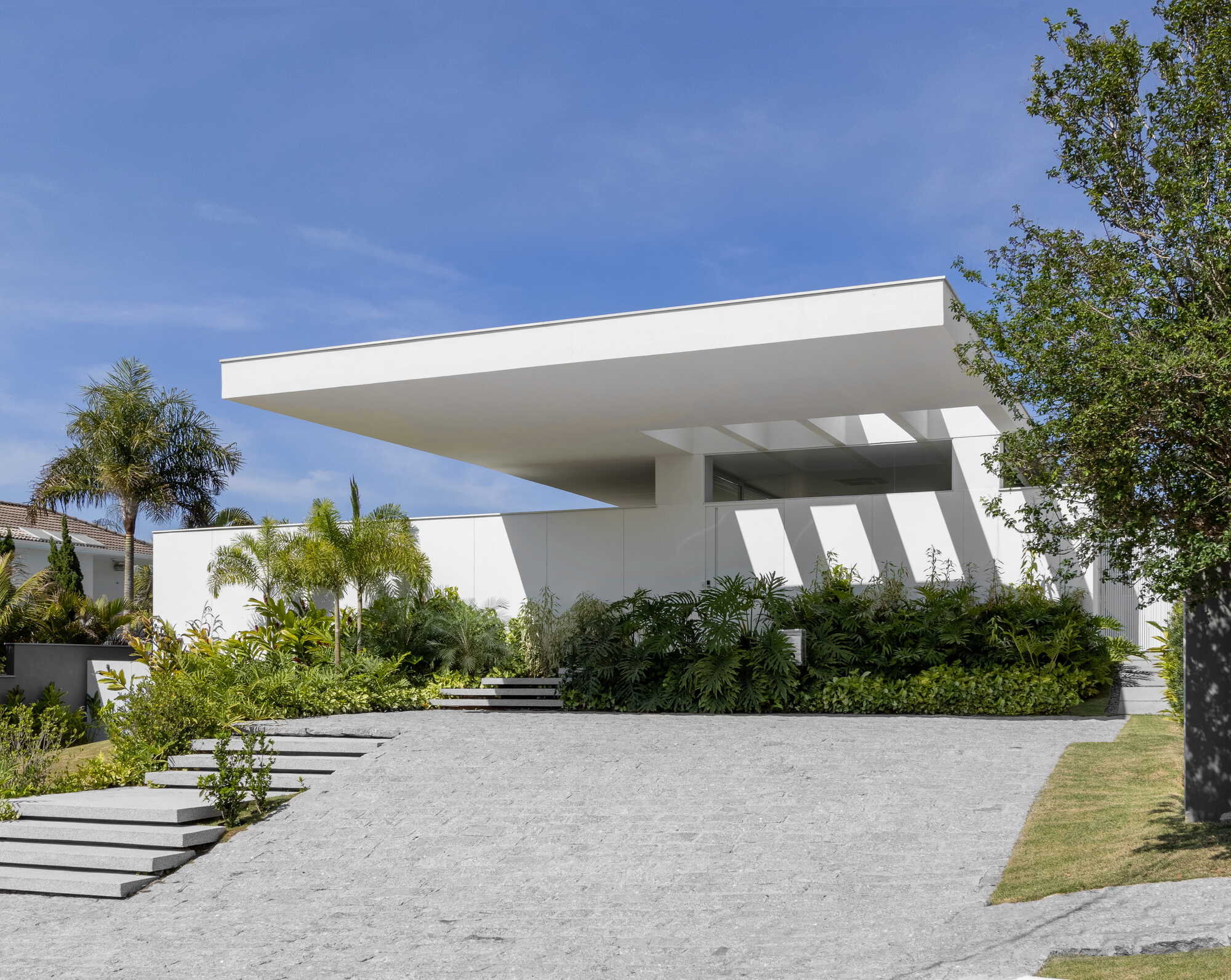 Entry facade with deep cantilevered roof plane and diagonal columns framed by palms