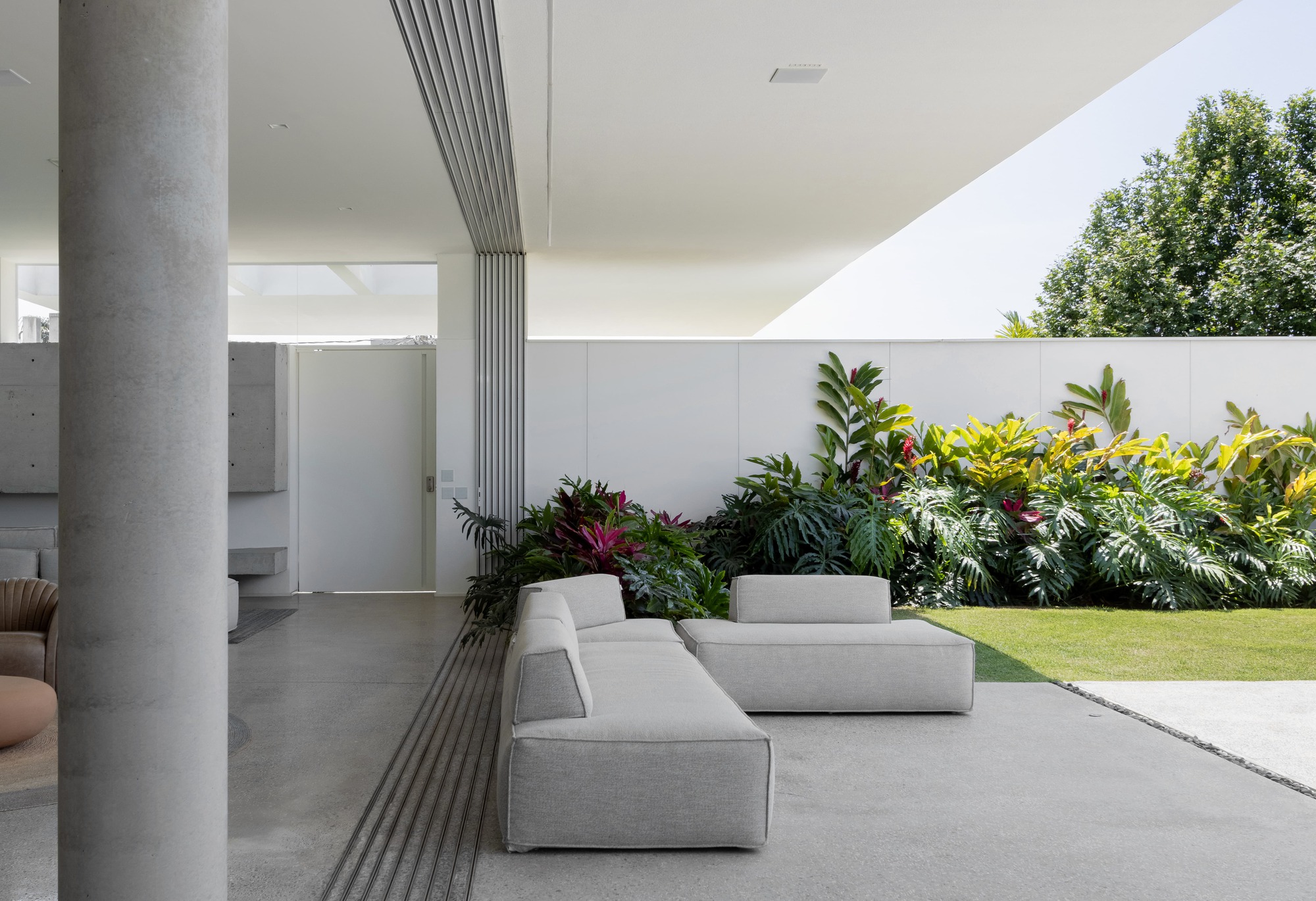 Outdoor seating area with grey lounge modules under a ribbed ceiling beam and lawn beyond