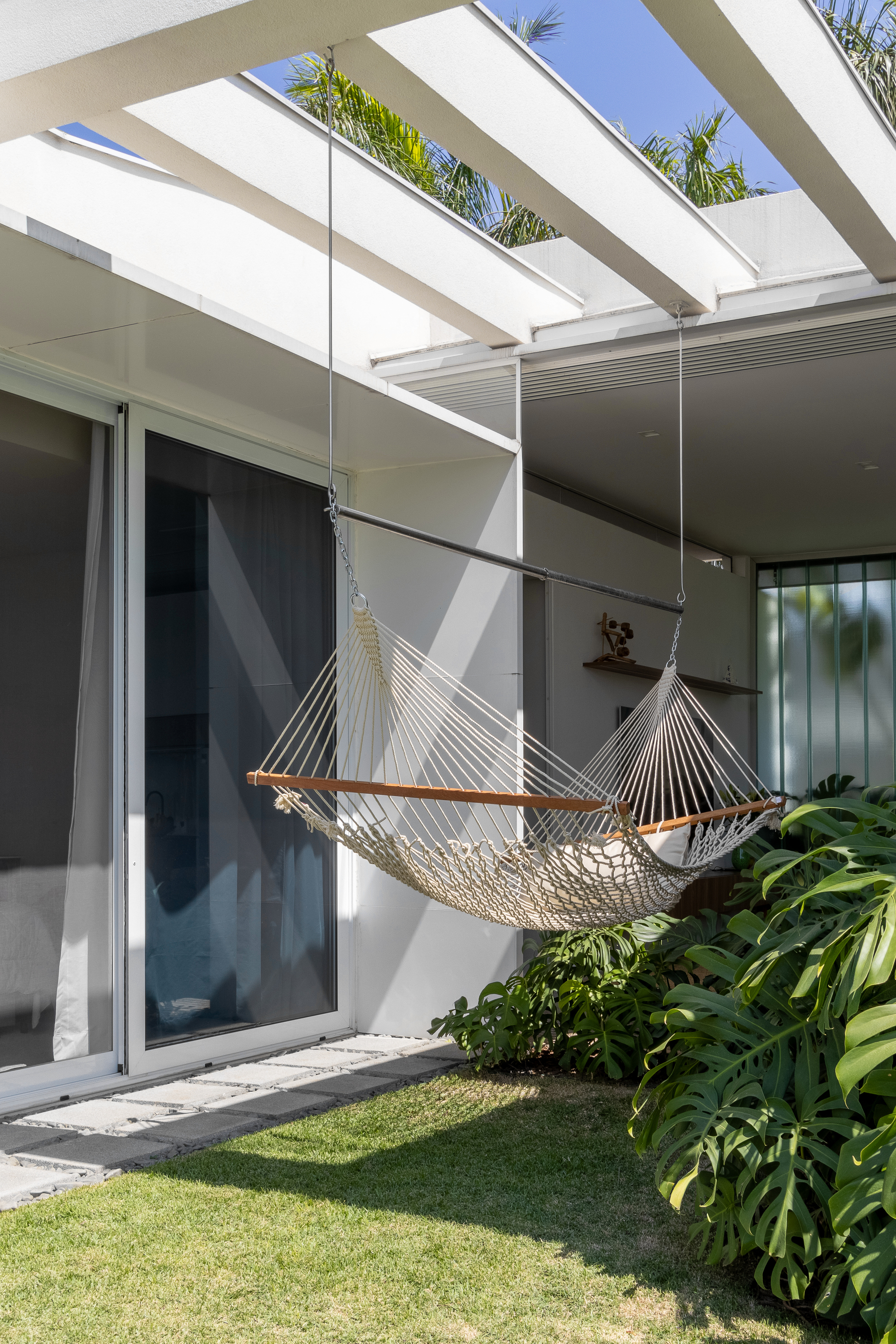 Covered courtyard with white structural beams overhead and a rope hammock suspended above the lawn
