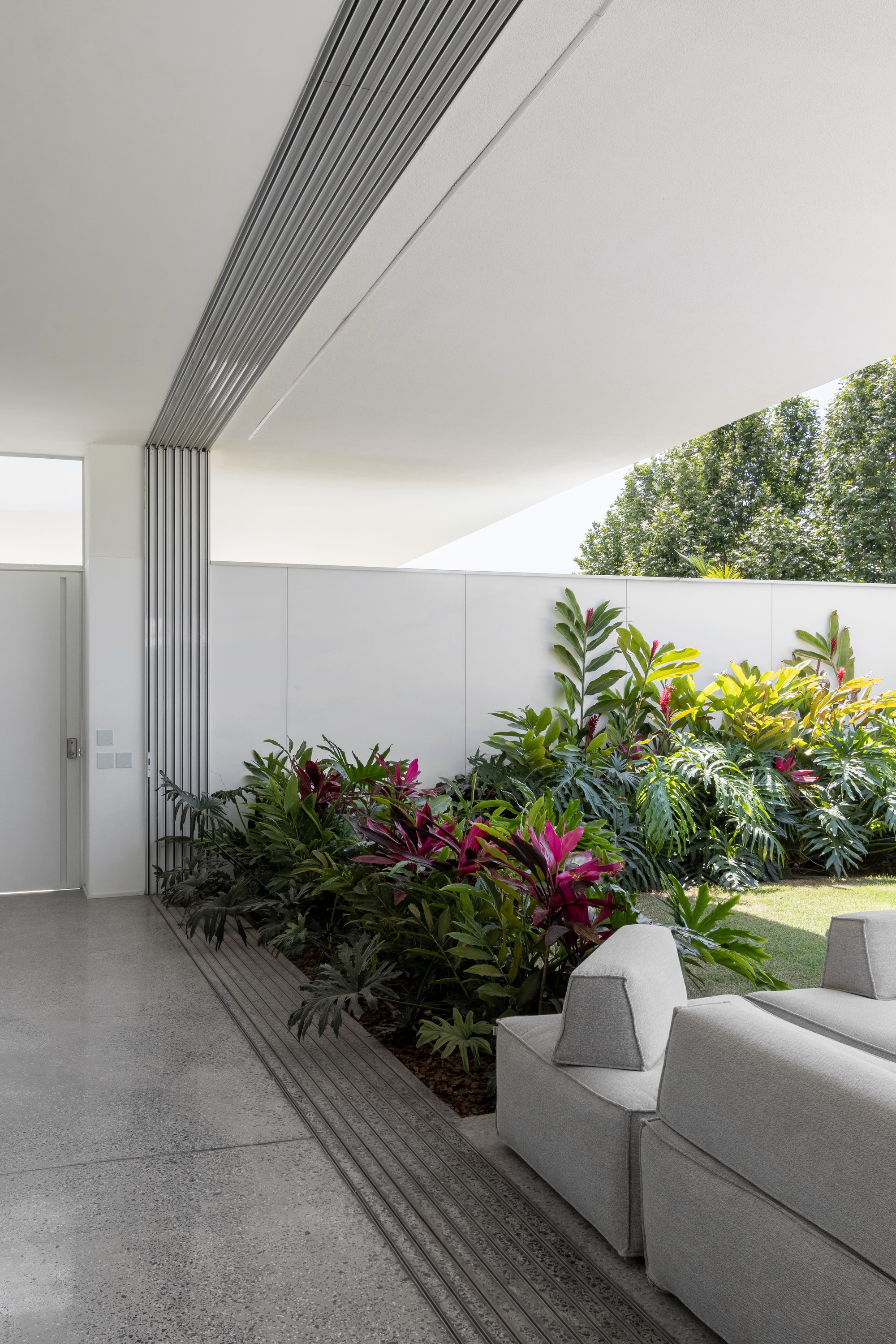 Interior courtyard with linear metal louvres meeting a planted bed of tropical foliage along the wall