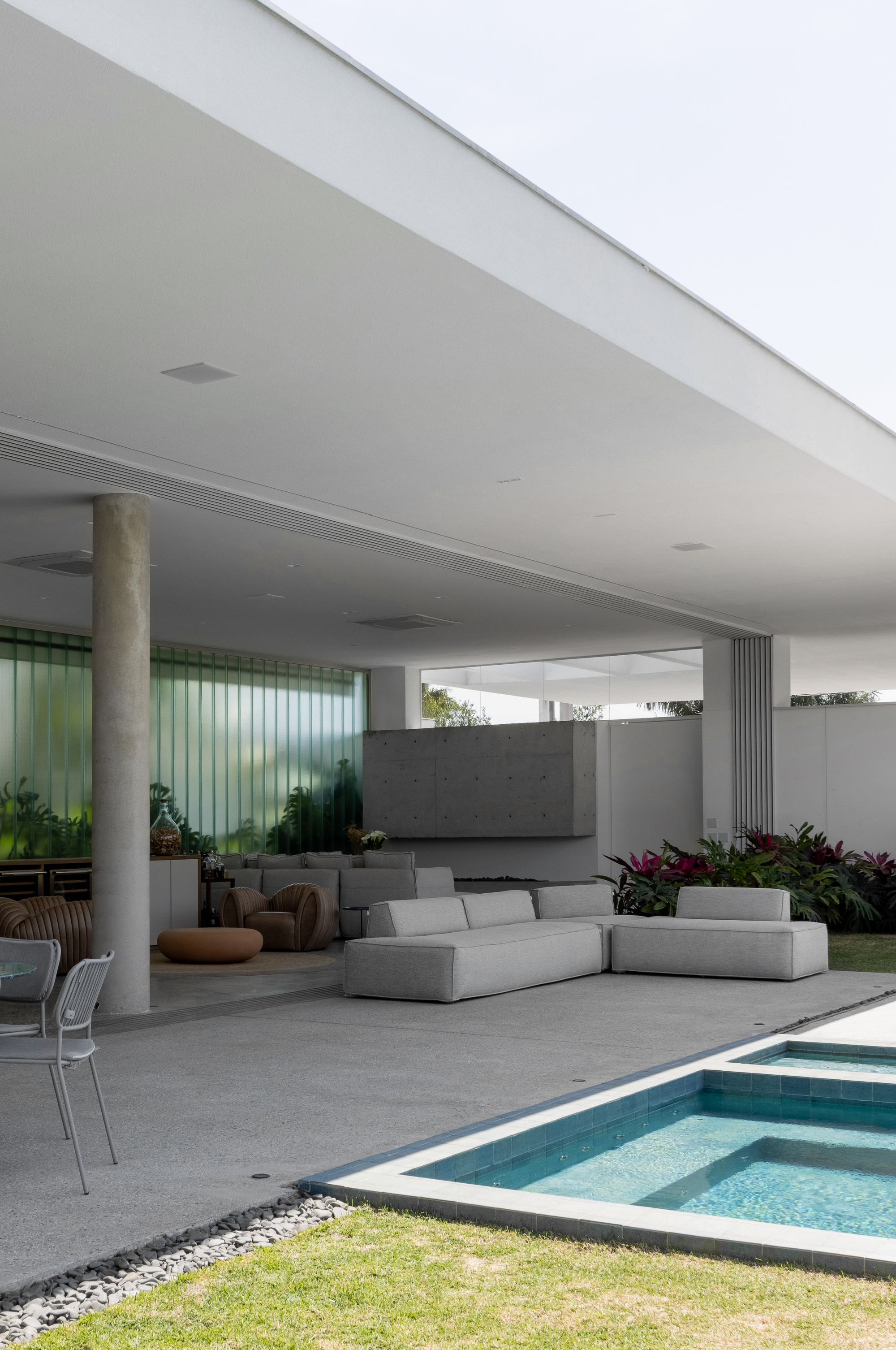 Covered terrace with concrete columns and ceiling overlooking a pool and lawn in bright daylight