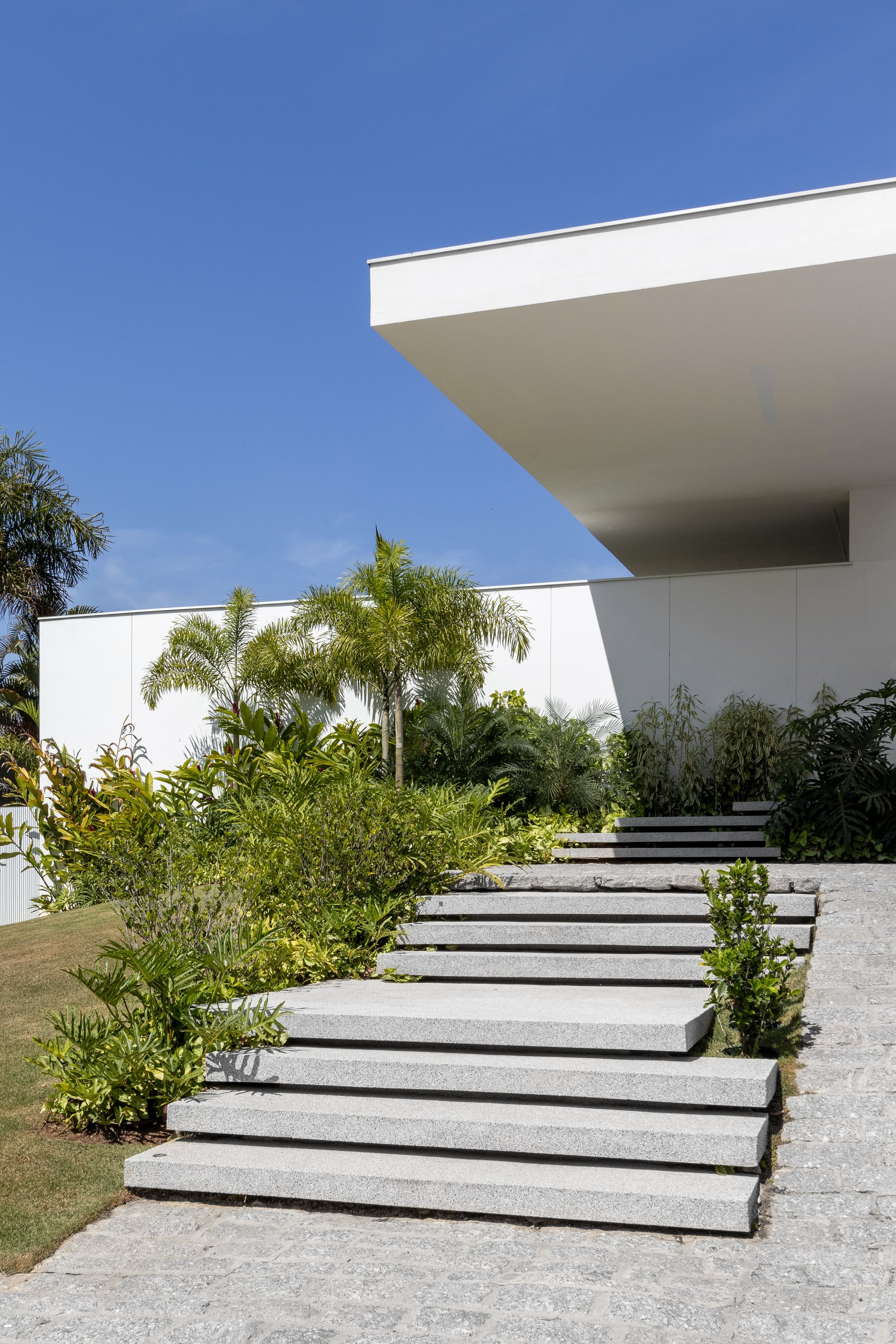 Floating concrete stepping pads rising through lawn and planting toward cantilevered white roof slab overhead
