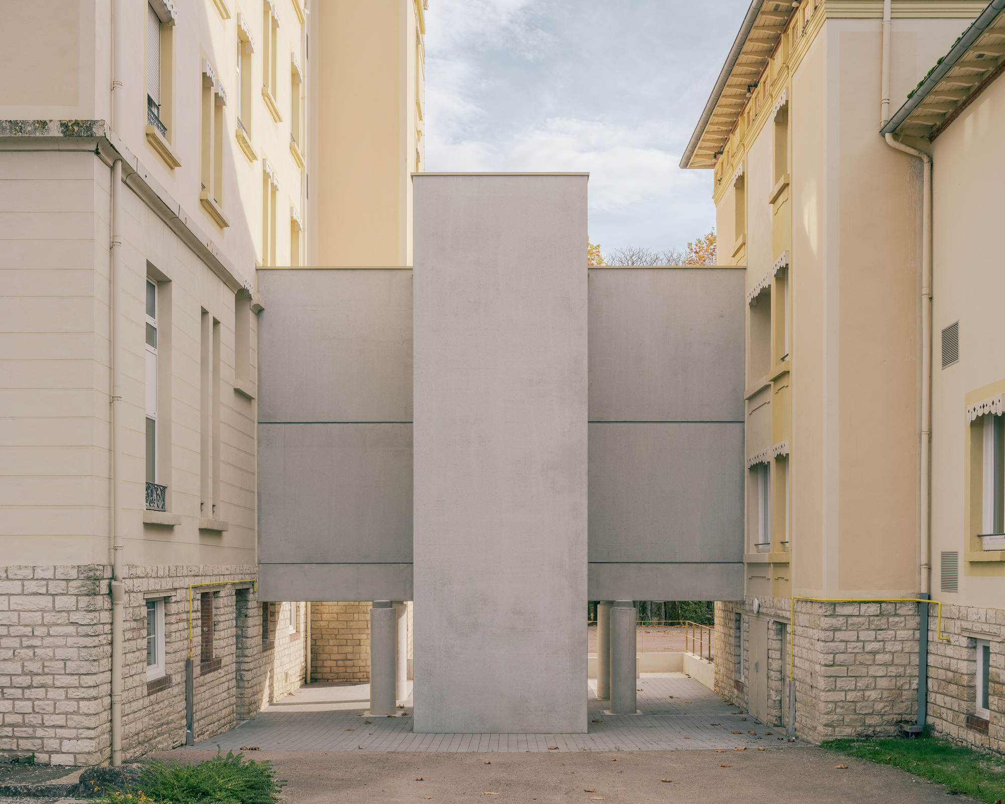 Courtyard view of stacked grey concrete panels raised on brick bases between plastered heritage wings