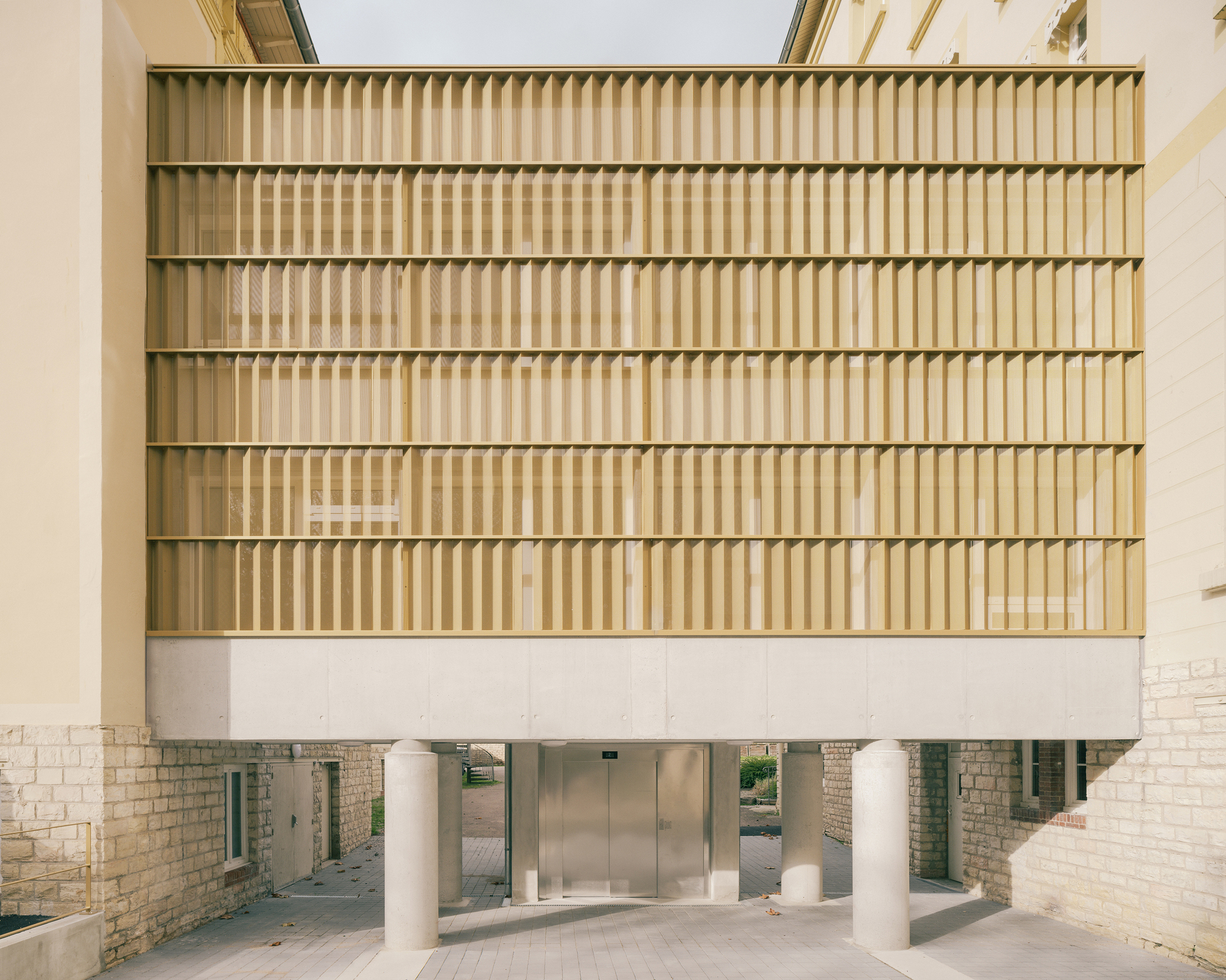 Head-on view of horizontal timber louvre facade lifted above a glazed ground floor on white columns