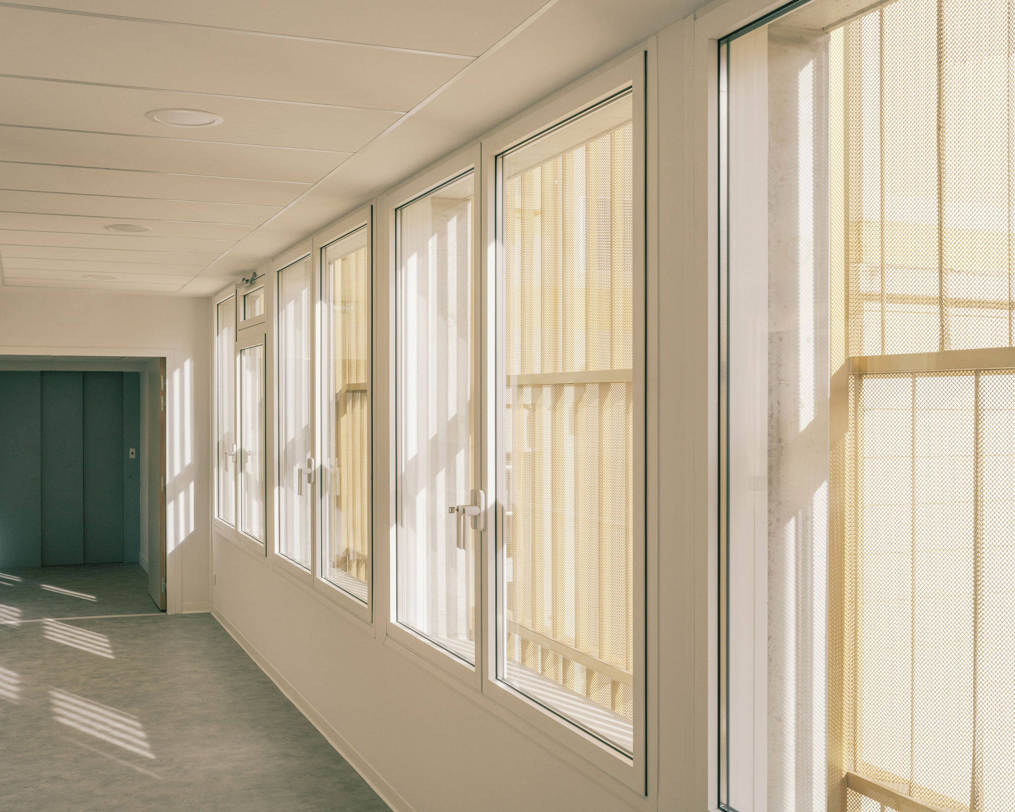 Interior corridor with timber-slatted doors and sunlight casting geometric shadows on the polished floor