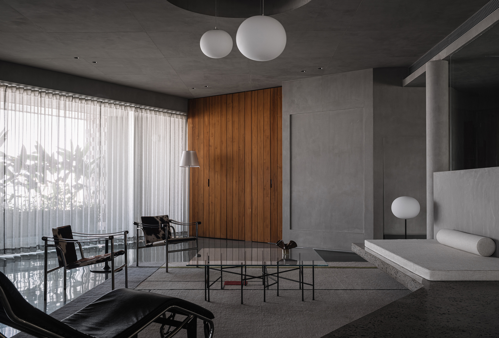 Living room with polished concrete floor, vertical timber door, and sheer curtains filtering daylight