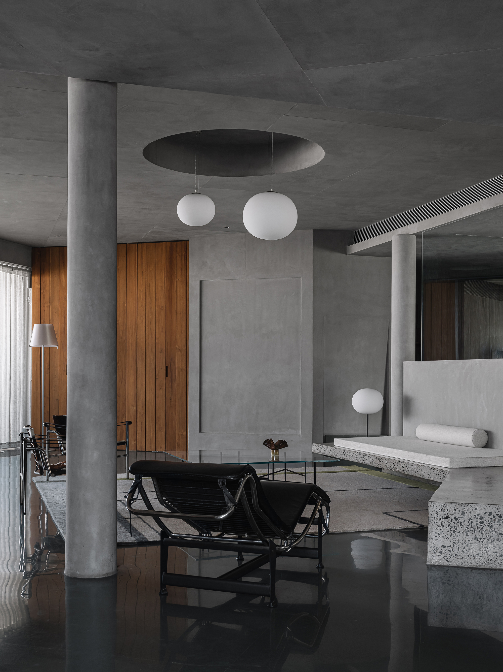Open living space with circular concrete column and recessed ceiling oculus above globe pendants
