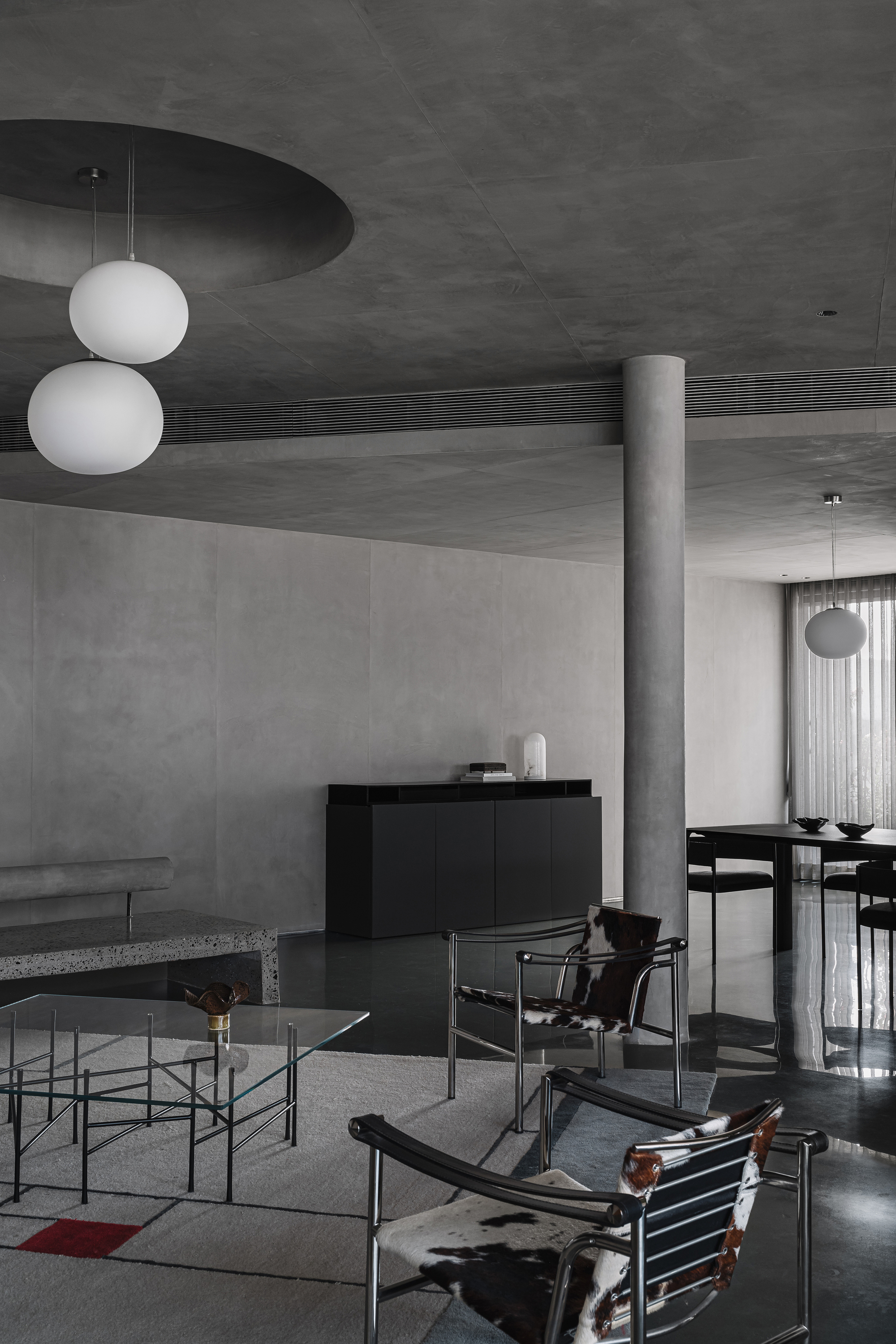 Living area showing concrete column, terrazzo platform, and spherical pendant lights beneath ceiling recess