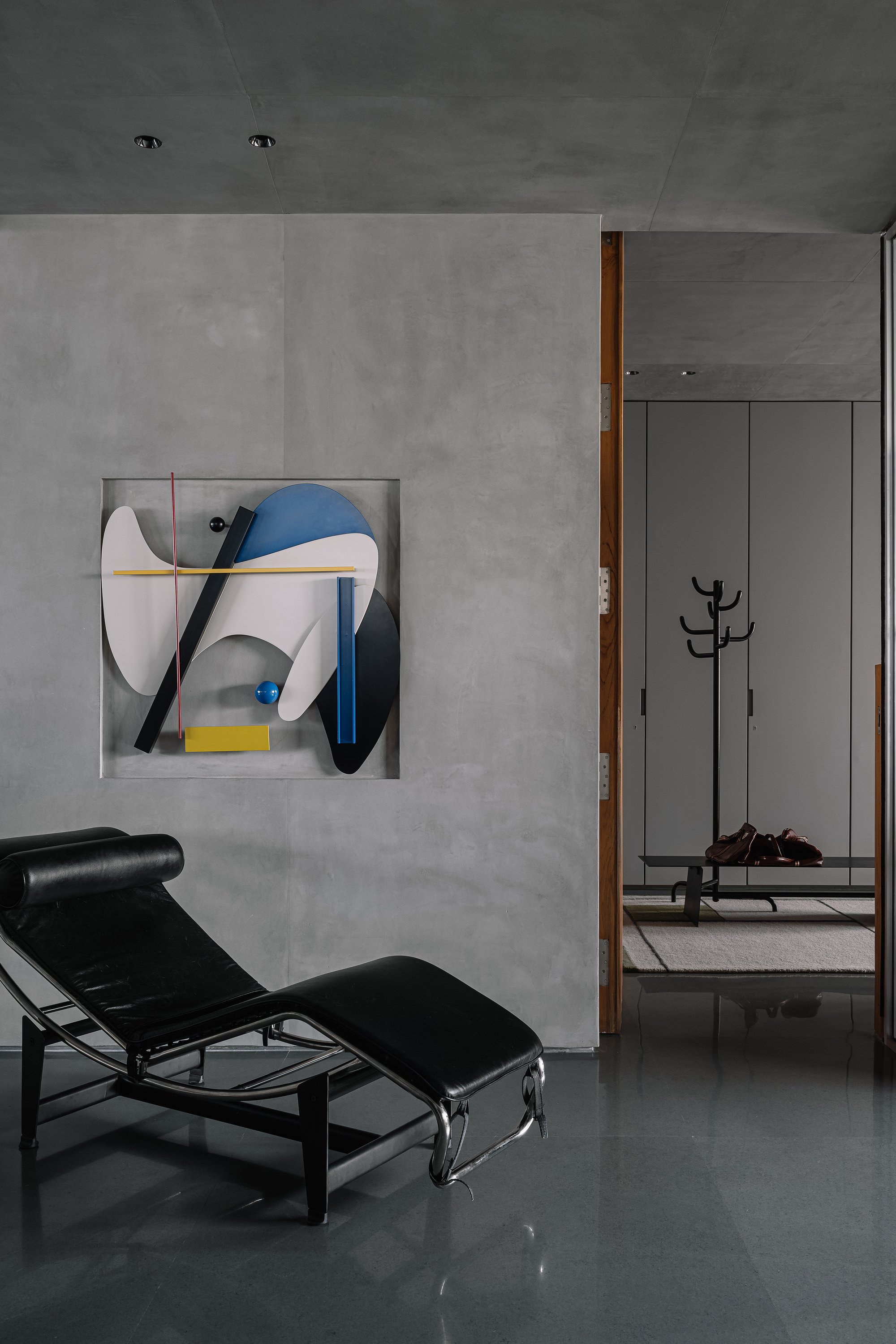 Concrete wall with abstract geometric artwork beside timber door opening to bedroom with coat stand