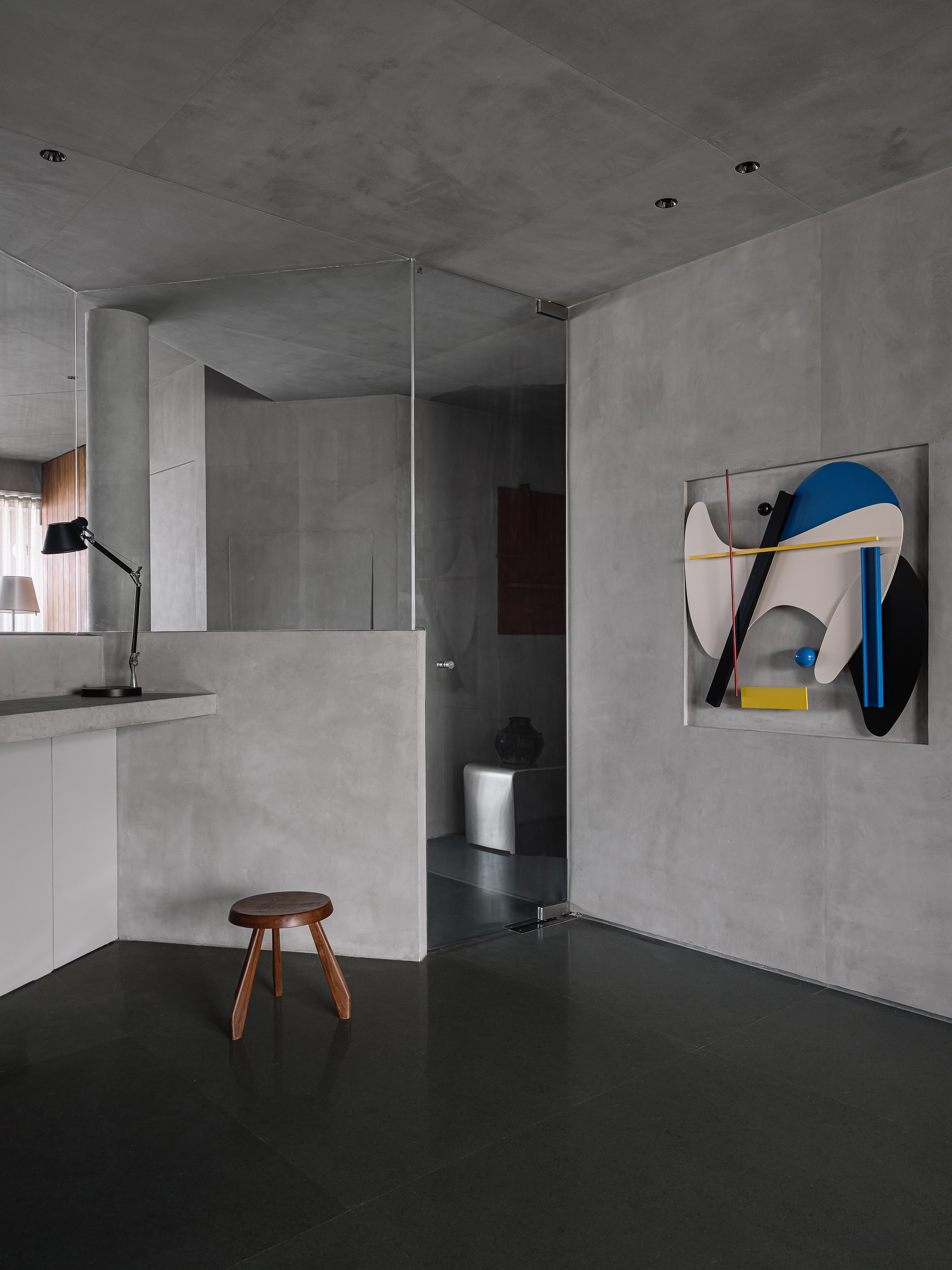 Open living area with concrete walls, dark resin floor, and abstract artwork beside glass partition