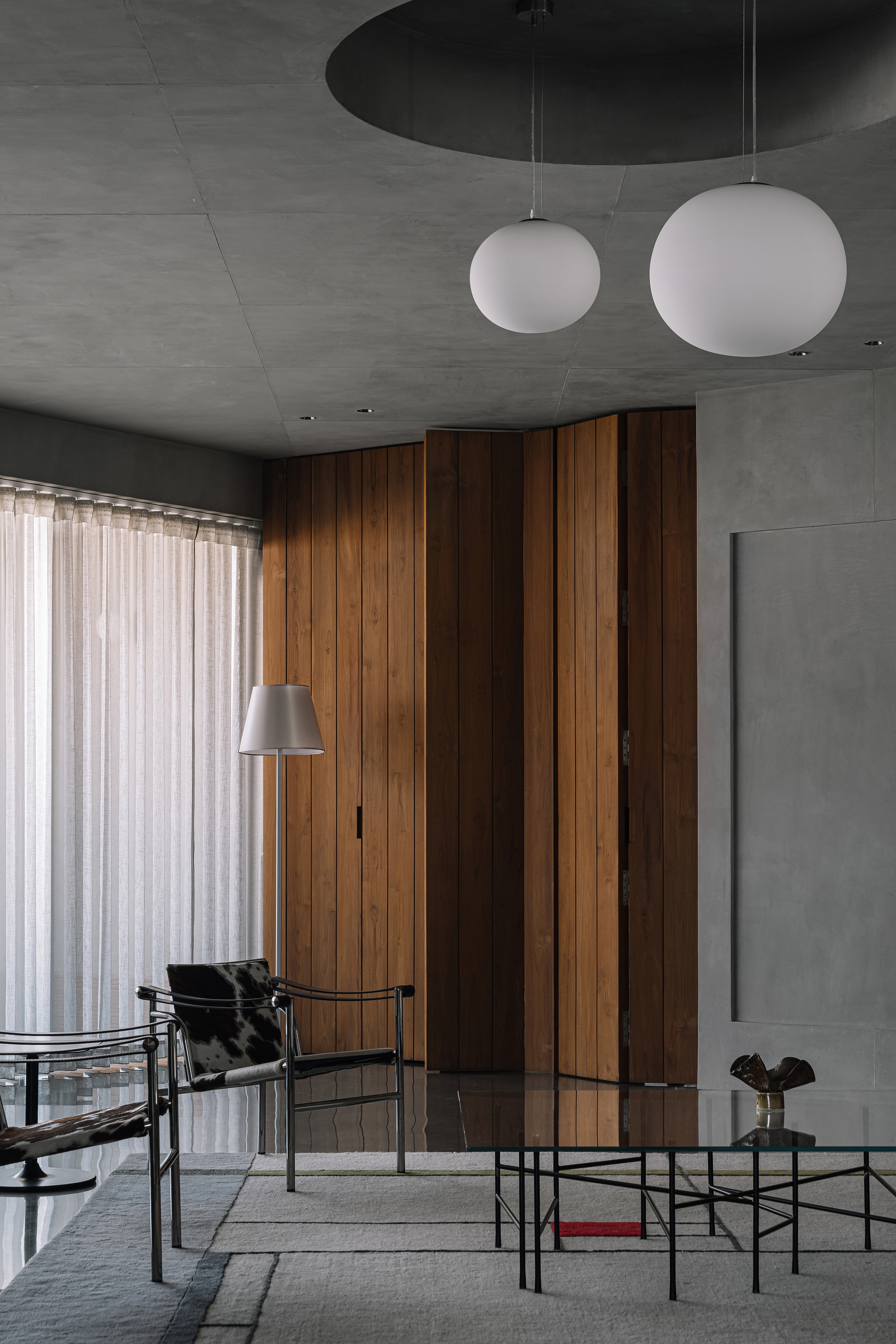 Living space with vertical timber wall panels beneath exposed concrete ceiling and spherical pendant lights